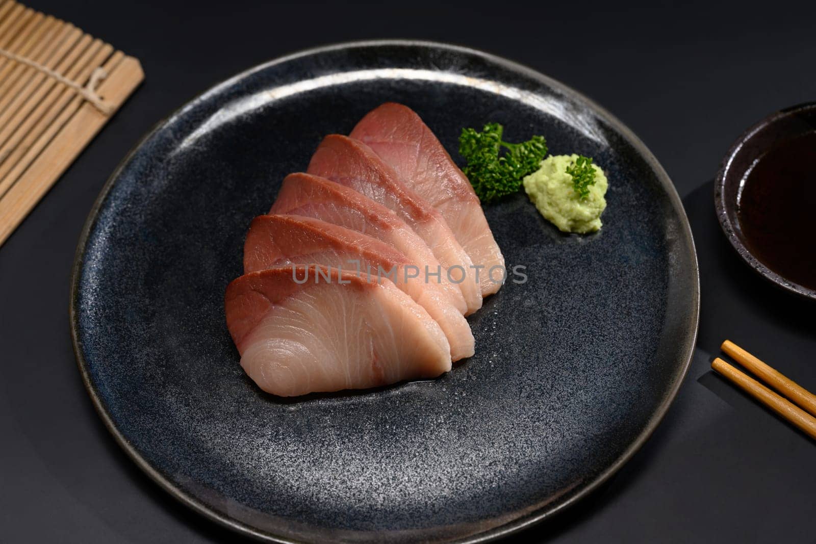 Fresh Hamachi sashimi on black plate with parsley leaf. Japanese food style by prathanchorruangsak