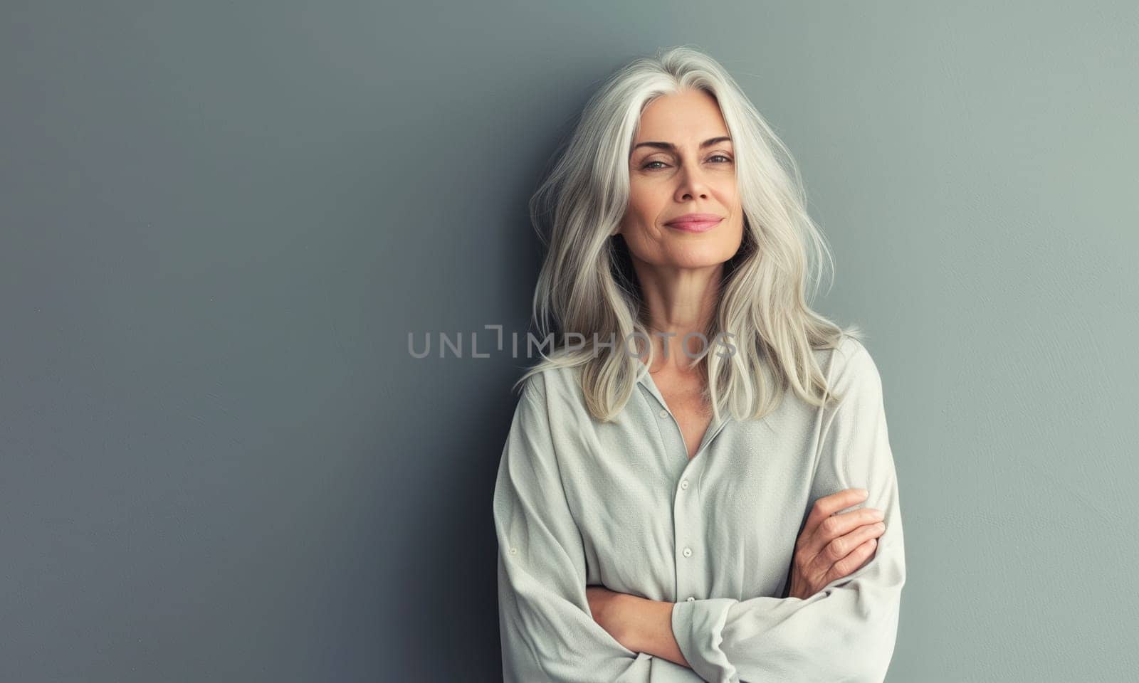 Fashion portrait of stylish senior woman with gray hair with crossed arms posing on gray studio background