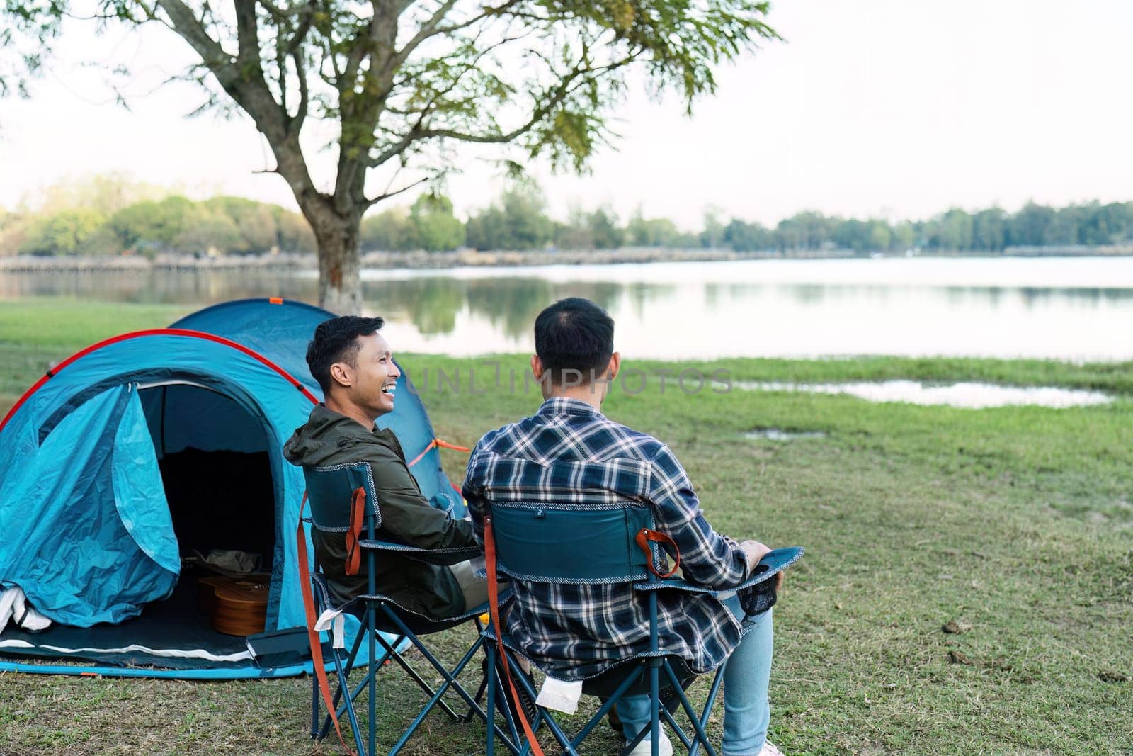 Gay LGBTQIA couple sitting on picnic chair drinking tea and coffee while camping on vacation holiday by itchaznong