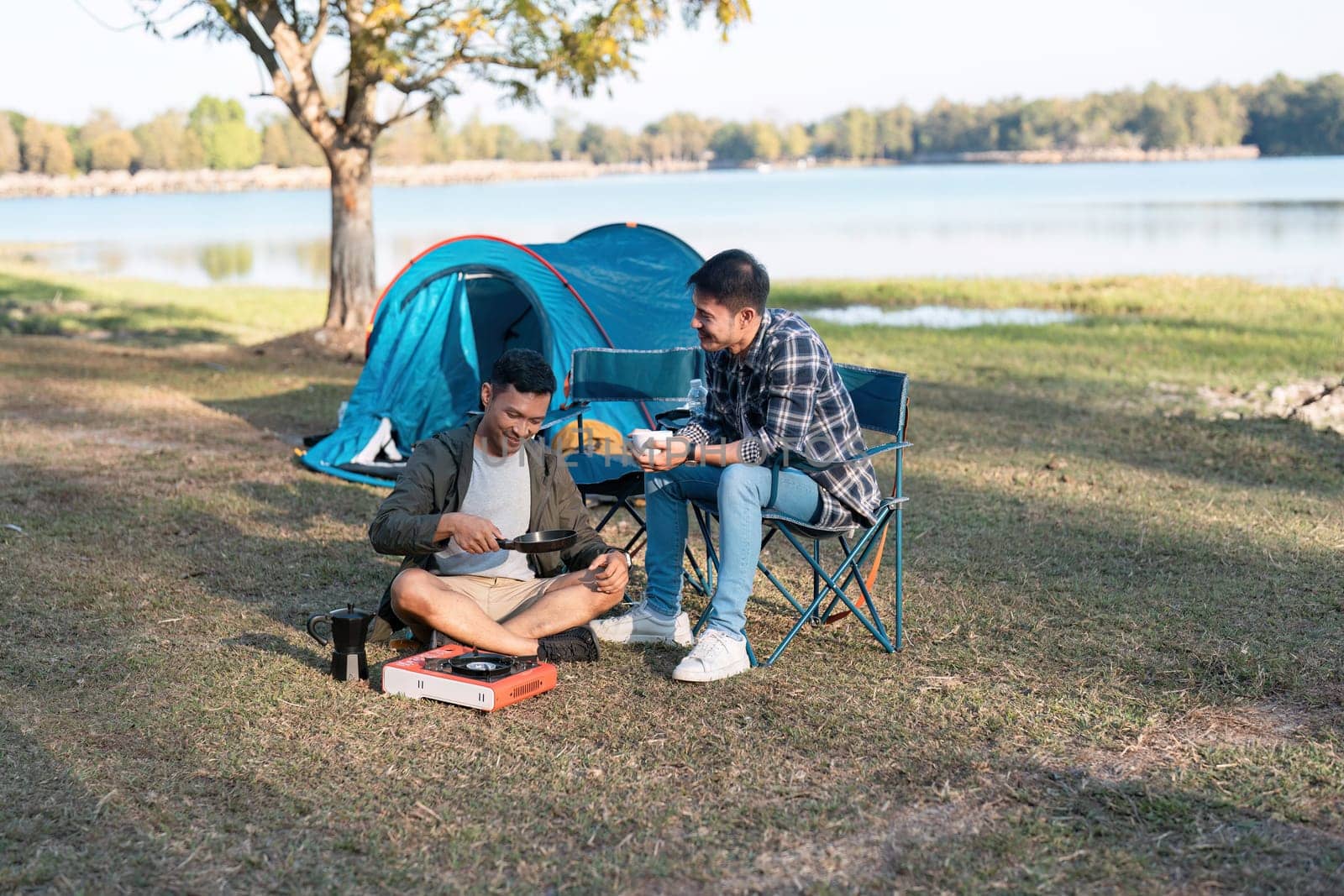 couple gay lgbt sitting in camp cooking and near river in mountains. Camping couple lgbt concept.
