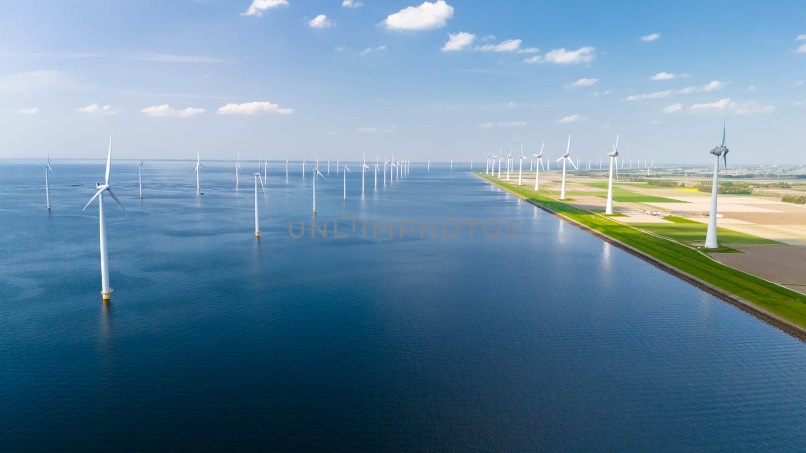 A serene scene of vast water surrounded by elegant windmills in Flevoland, Netherlands. The windmills stand tall, harnessing the power of the wind to generate energy by fokkebok