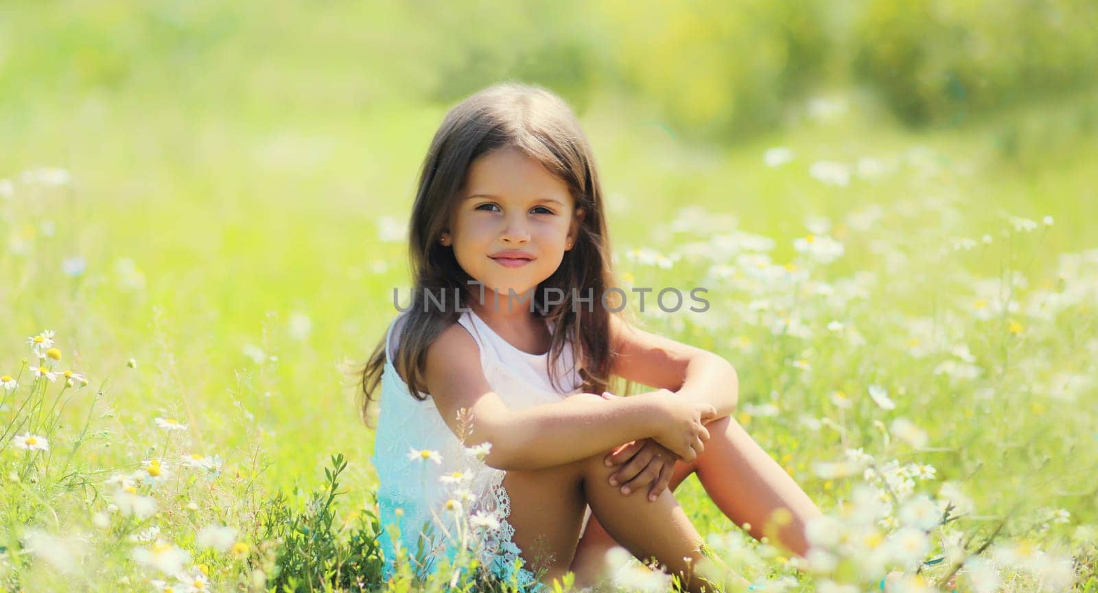 Portrait of happy little girl child sitting on grass in sunny summer park