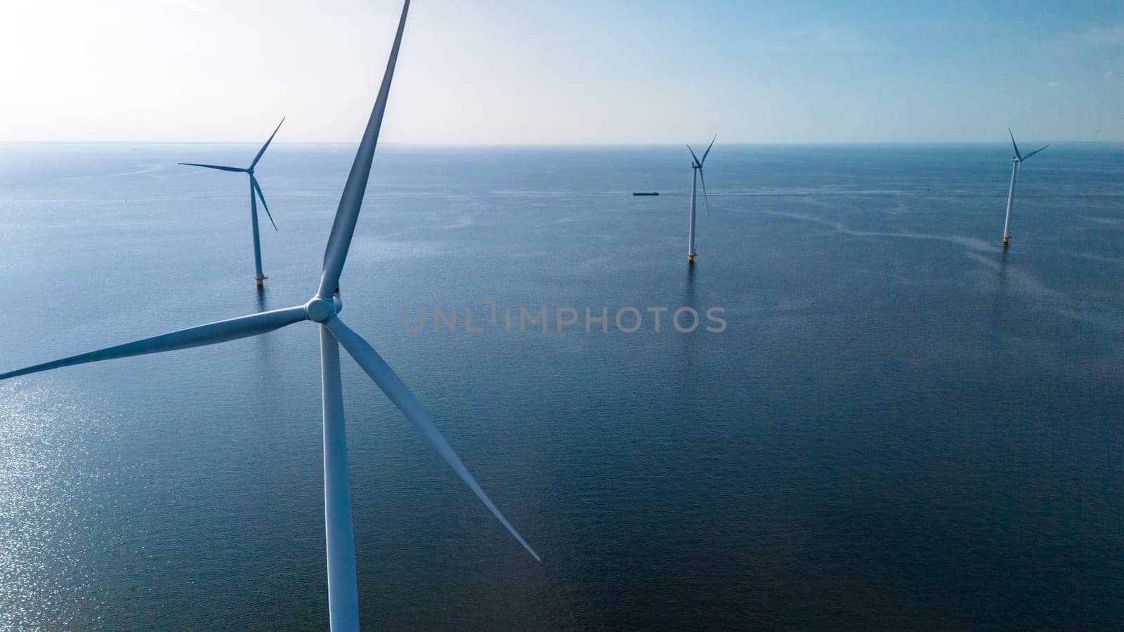 A group of majestic wind turbines stand tall in the ocean, their blades gracefully turning in the wind to generate clean, renewable energy by fokkebok