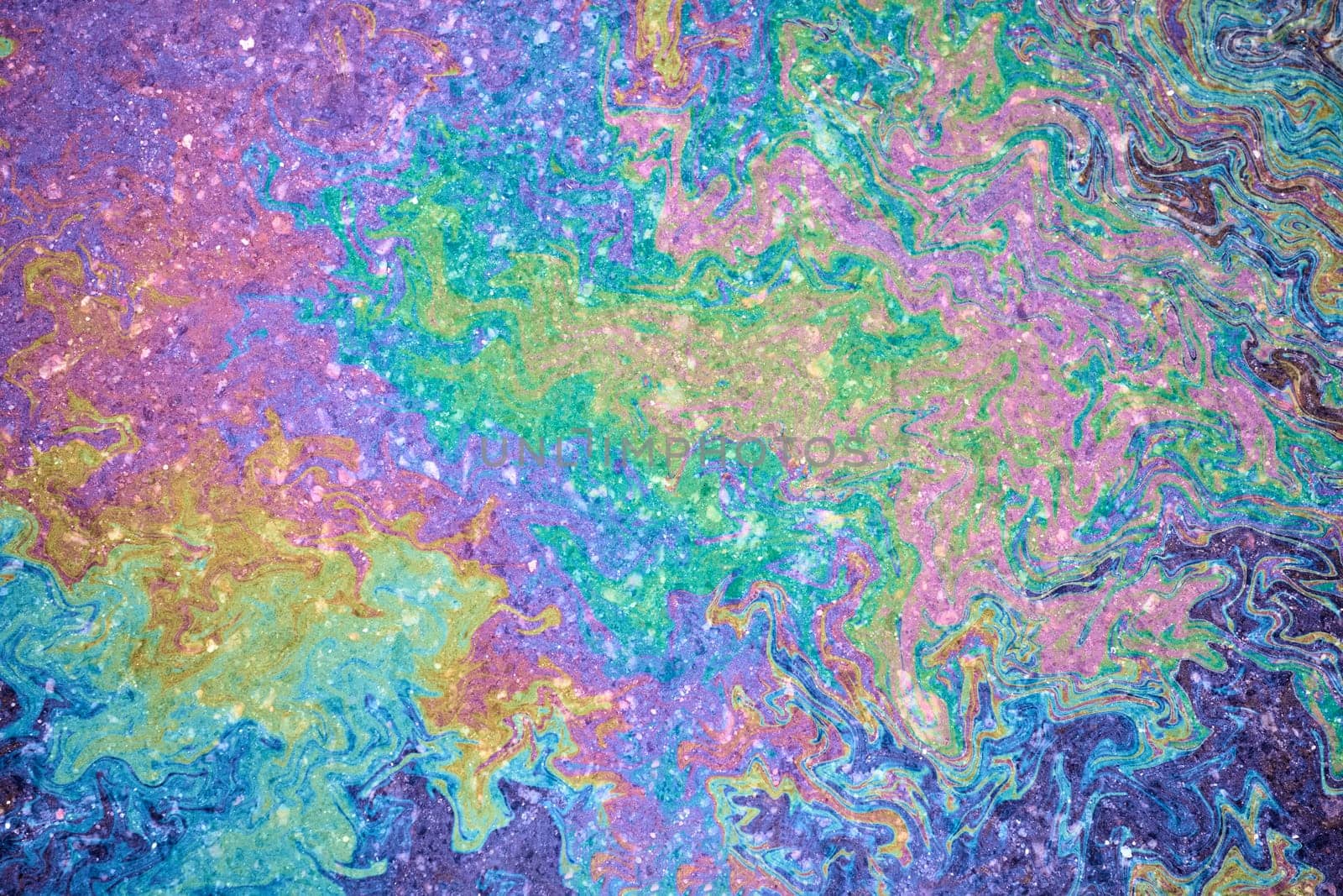 An overhead shot of the mesmerizing patterns created by leaking gasoline on wet ground