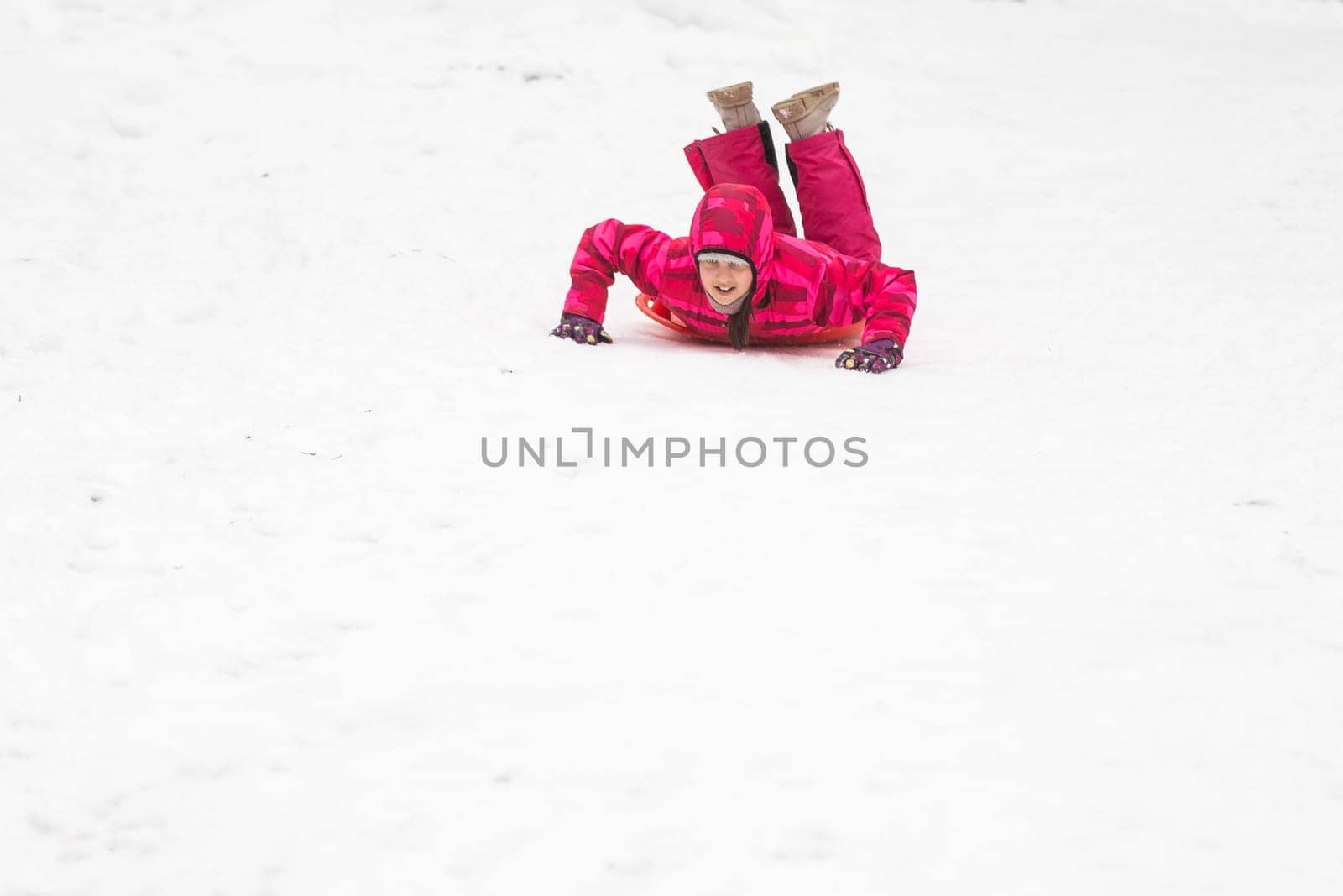 childhood, sledging and season concept - happy little girl sliding down on sled outdoors in winter. High quality photo