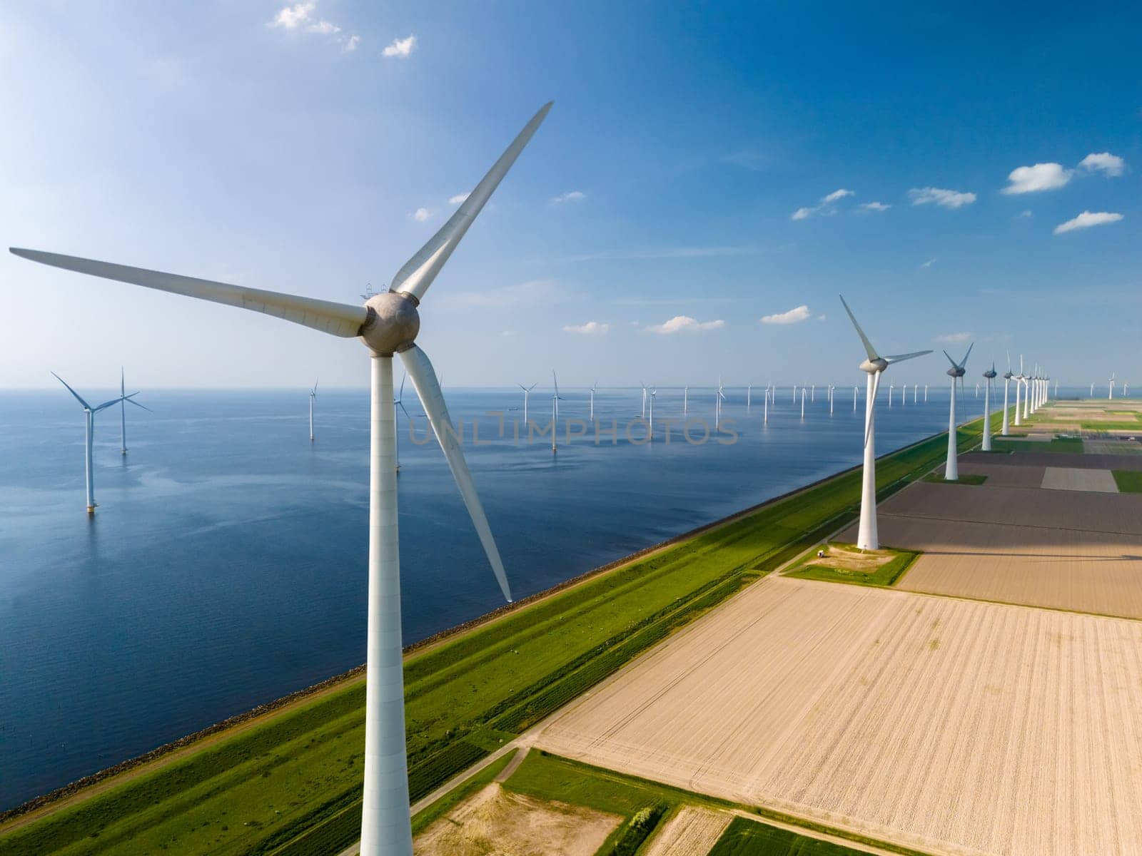 A line of towering wind turbines standing proudly next to the tranquil waters of Flevoland in the Netherlands.