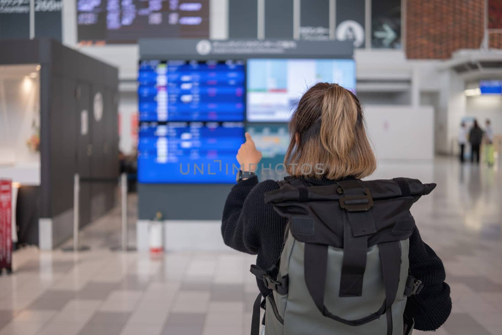 Young Asian woman in international airport looking at flight information board, checking her flight.