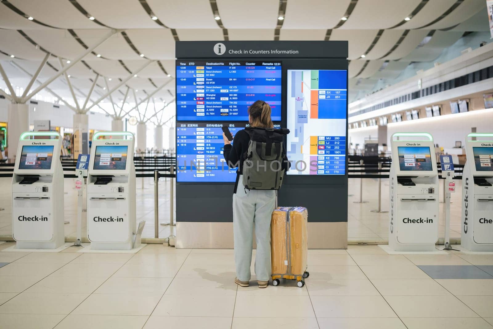 Young Asian woman in international airport looking at flight information board, checking her flight.