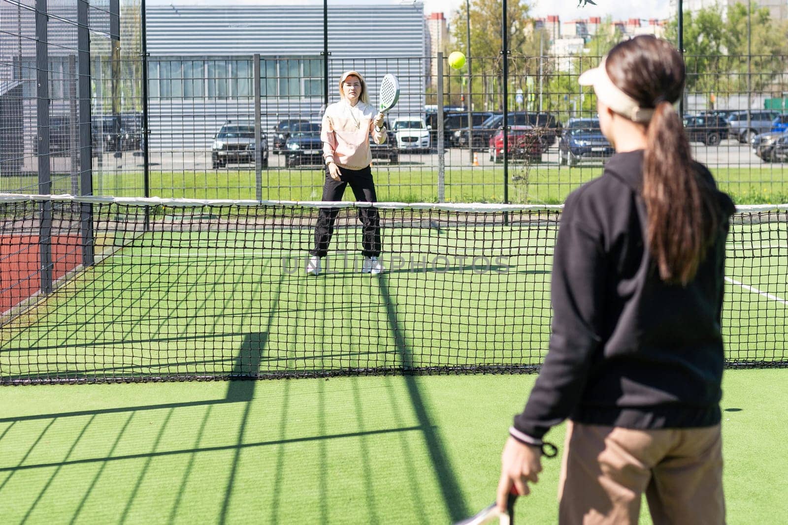 positive mother and daughter standing on court with padel rackets. High quality photo