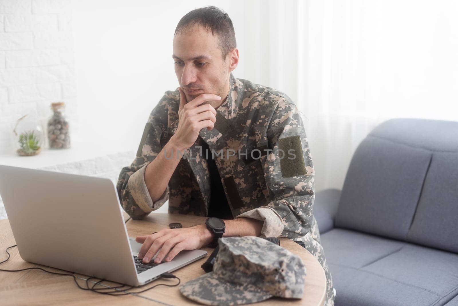Young hispanic man army soldier using laptop sitting on table at home. High quality photo