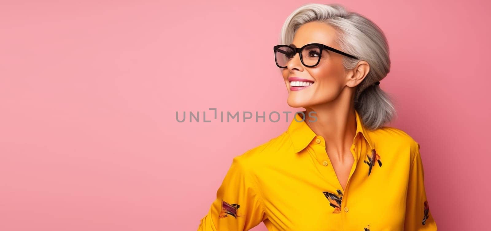 Fashion portrait of stylish happy smiling mature woman with gray hair in bright colorful clothes posing on pink studio background