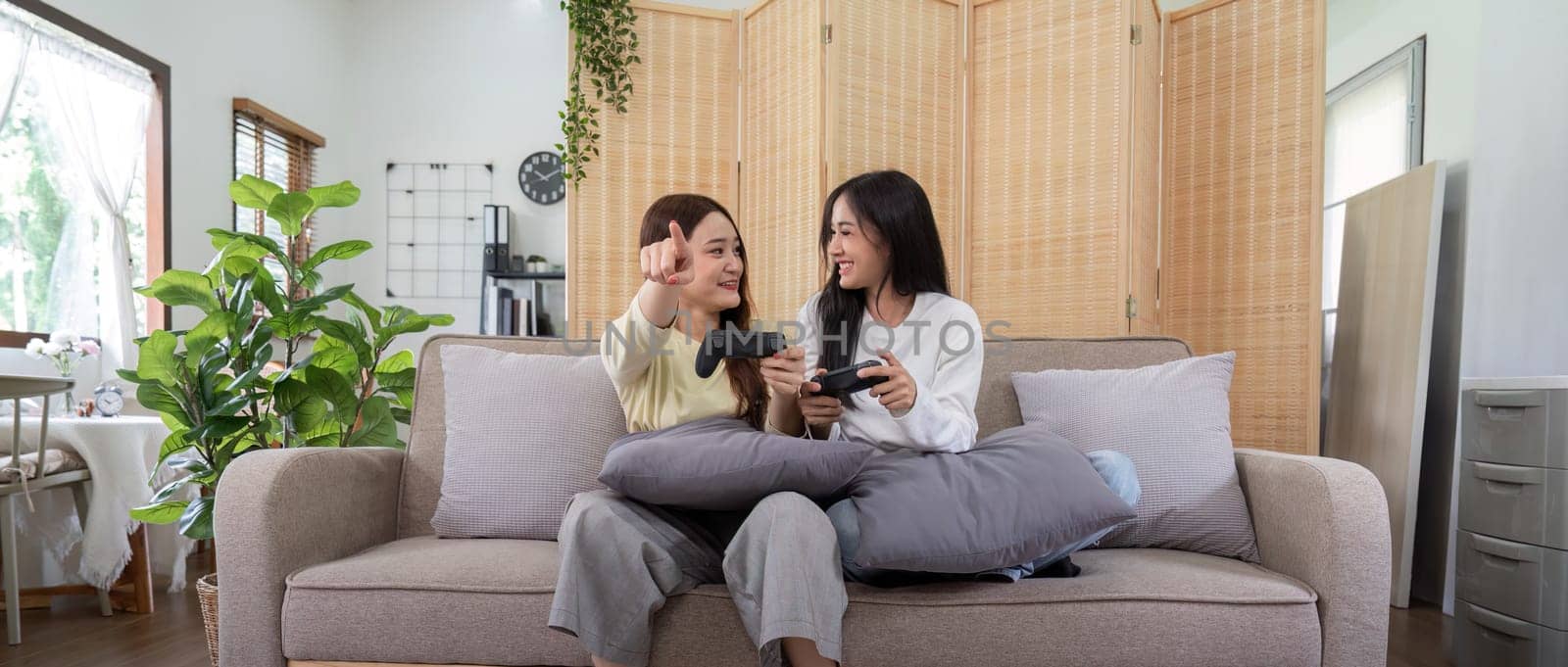 Happy LGBT lesbian couple holding joystick and playing video game in relax day by nateemee