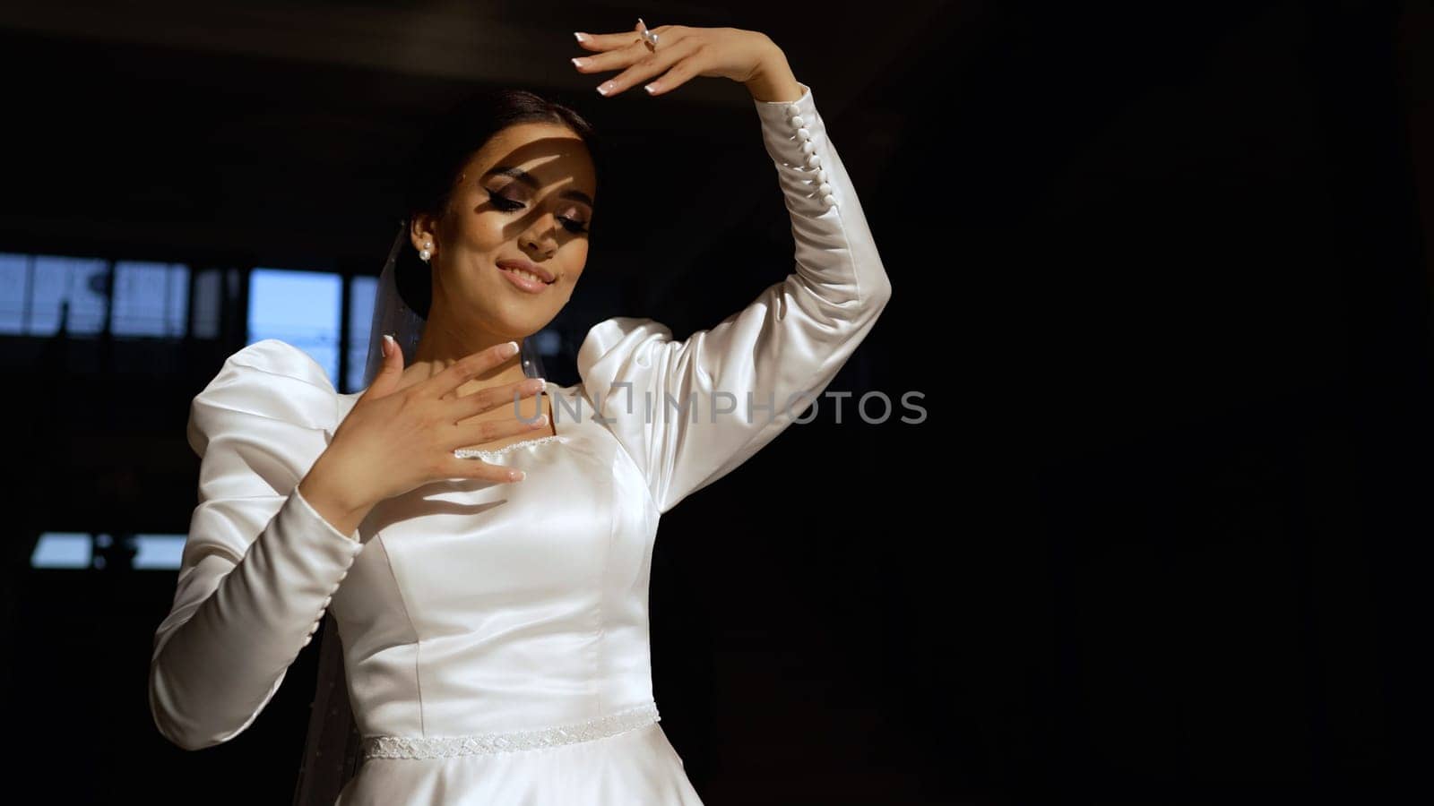 A beautiful bride under a veil dances in the rays of the sun. A young brunette in a white dress dances in the sun. Young woman in a dress. Turkish bride, close-up of face.