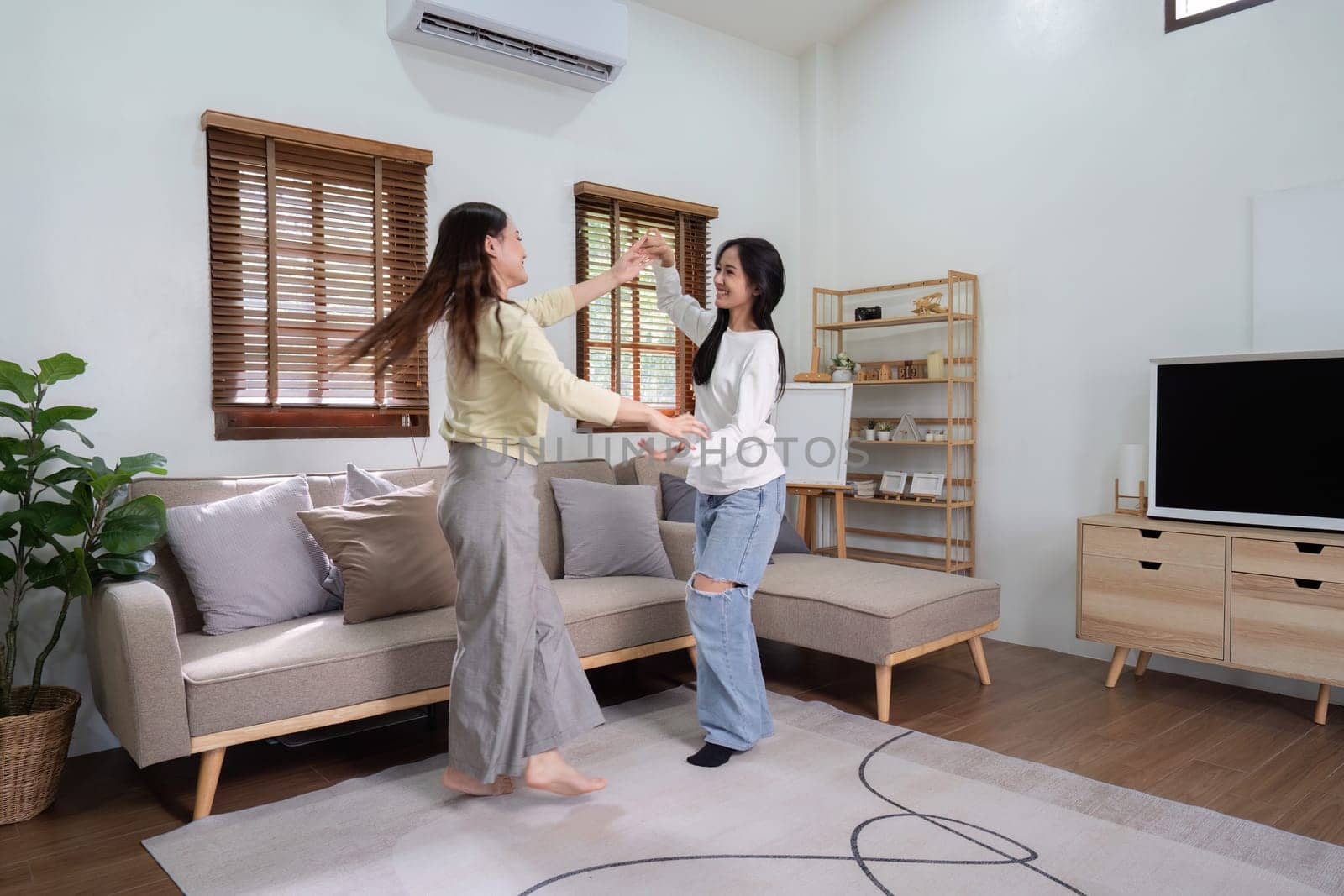 Lesbian asian couple dancing with each other while resting at the living room.