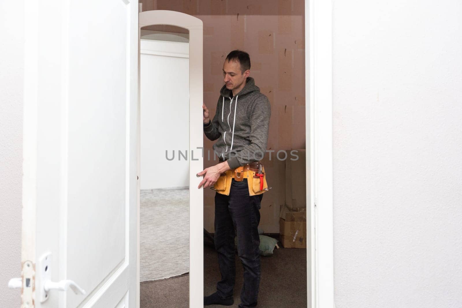 Young caucasian brunette man standing half sideways,holding with hands the middle door of a closet with a mirror to set,close up side view with selective focus. Furniture assembly concept. High quality photo