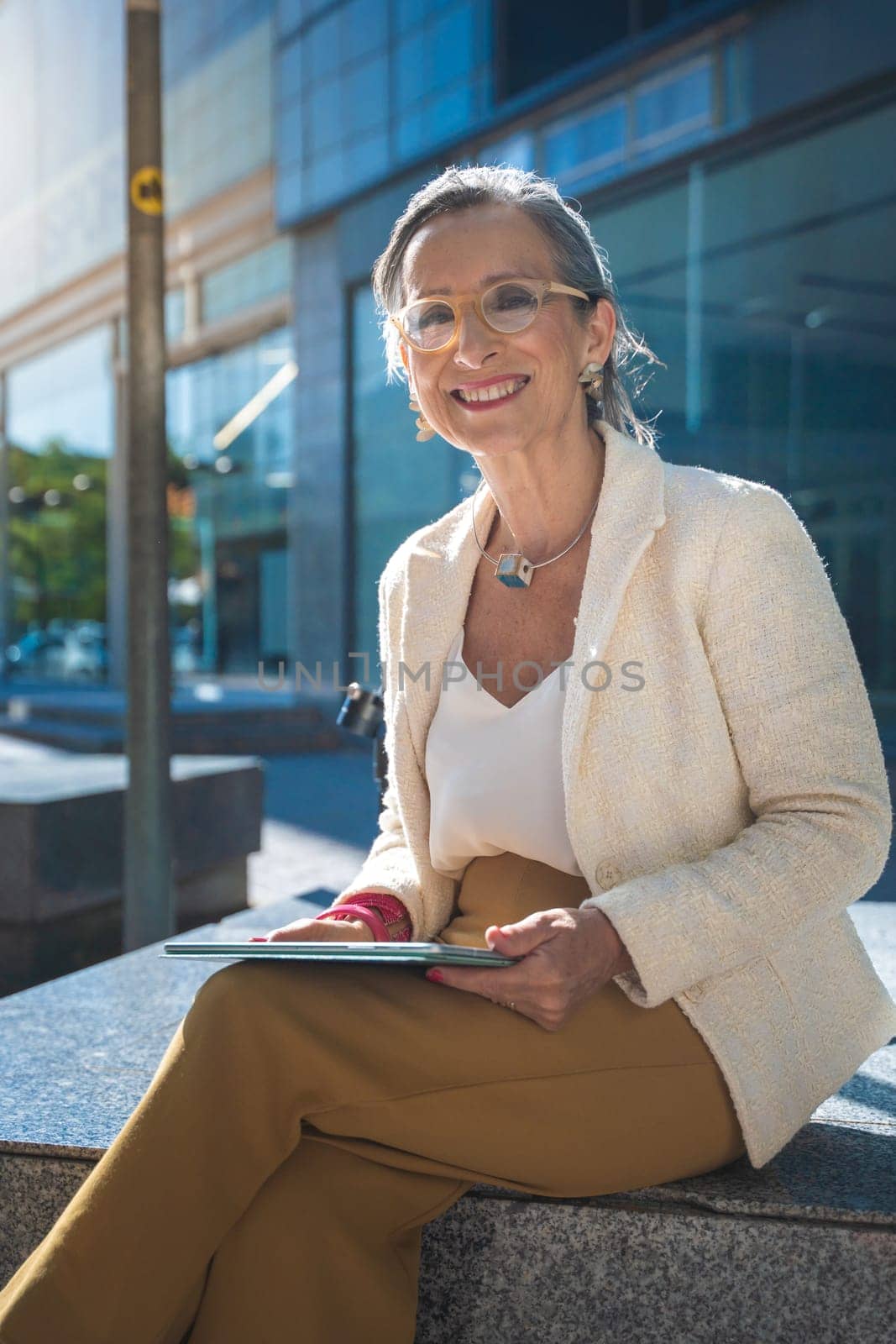 Happy attractive business woman middle-aged looking to camera smiling with technology tablet in front of a modern building. High quality photo