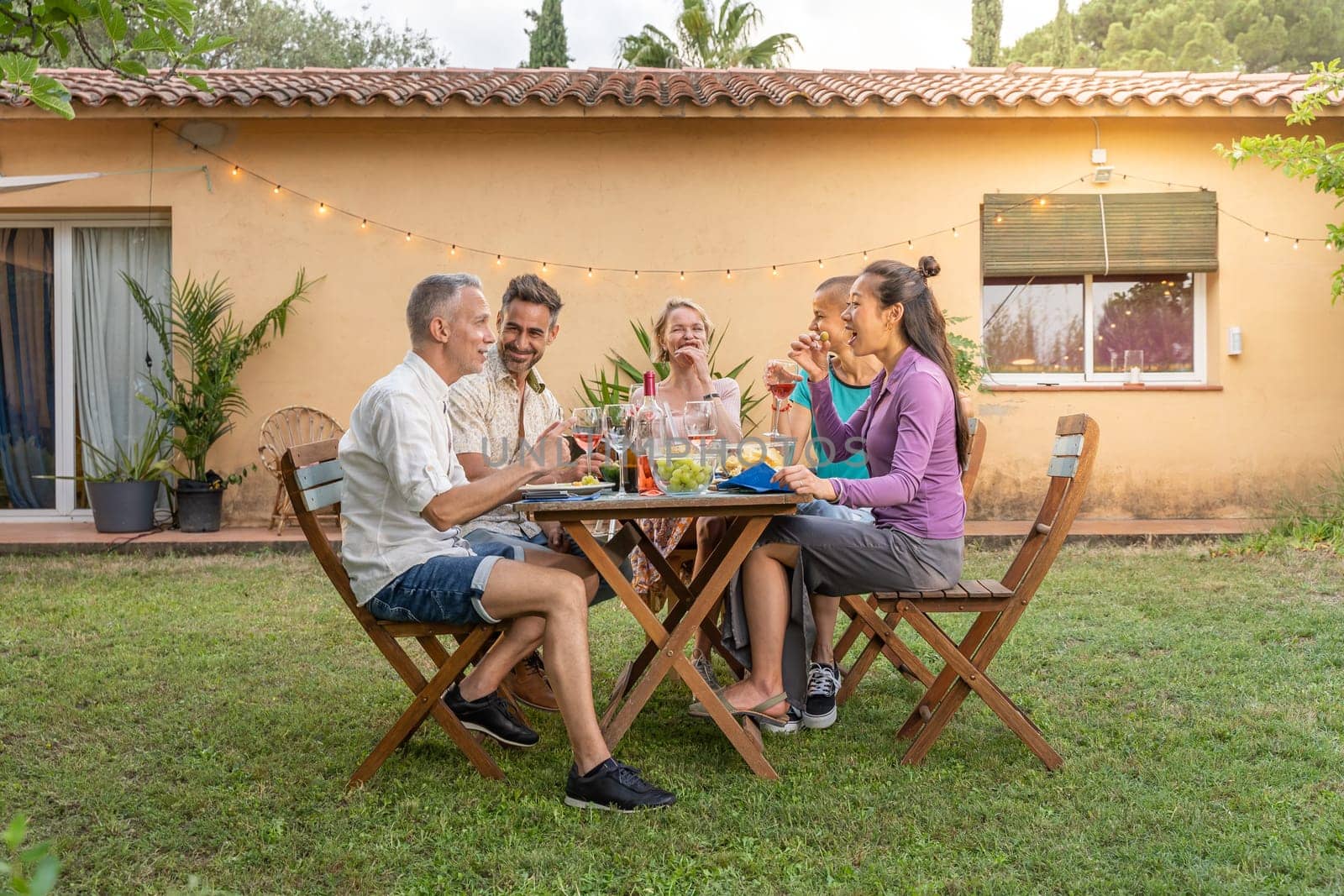 Group of multiethnic friends eating and drinking happy smiling and laughing in the patio. Middle-aged cheerful people around the table. by PaulCarr