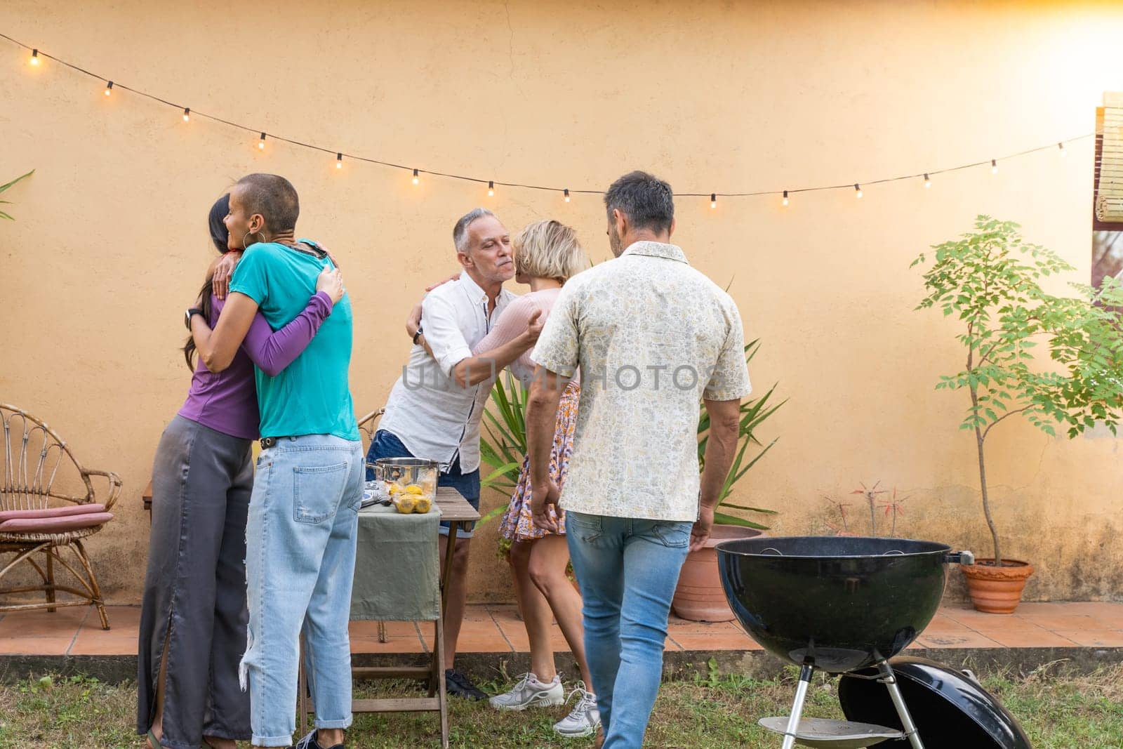 Multiethnic middle aged men and women friends greet each other and huddle together happily in barbecue in backyard. by PaulCarr