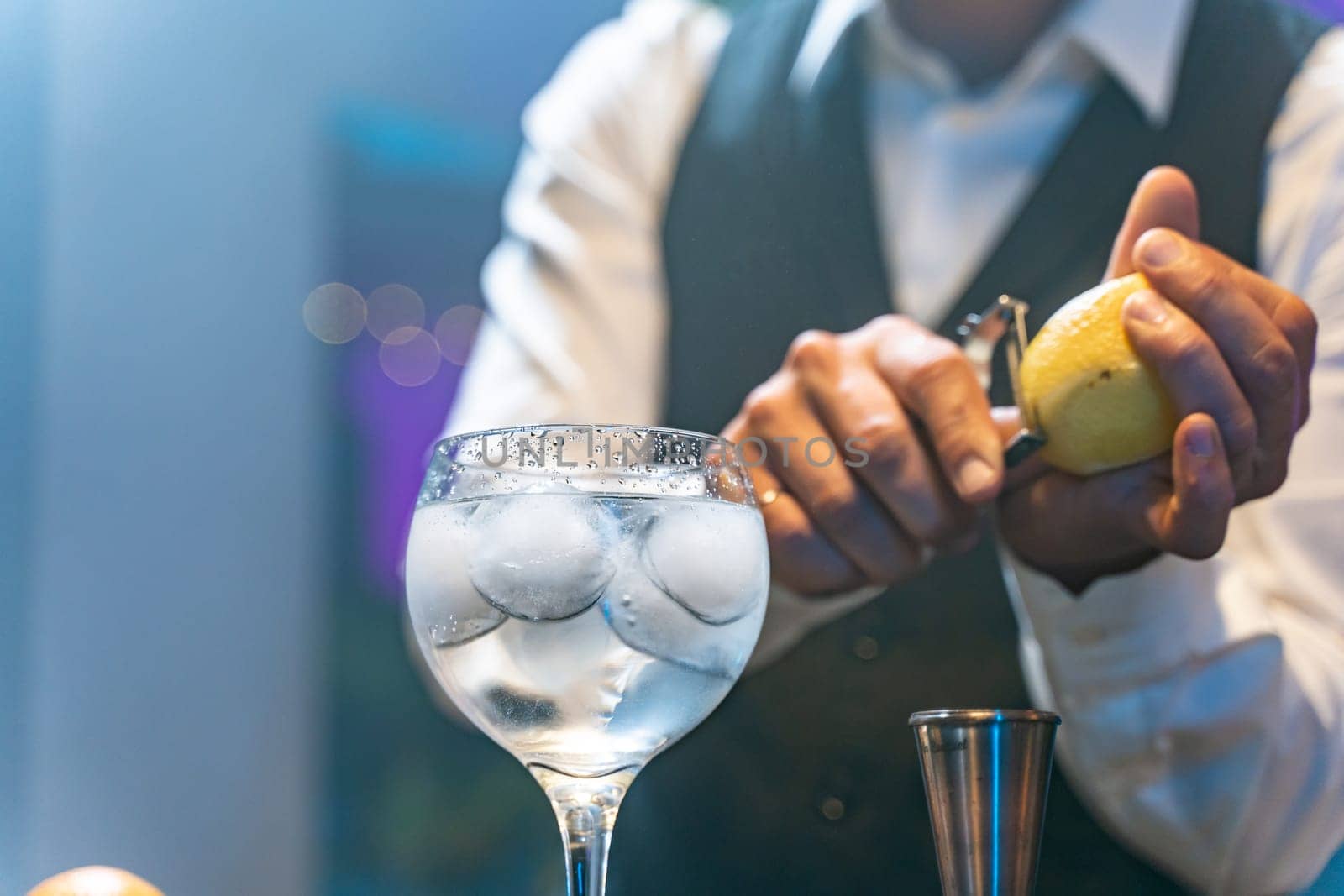 Professional barman in a white shirt and black apron making cocktail with lemon at party in nightclub. Nigh life. High quality photo