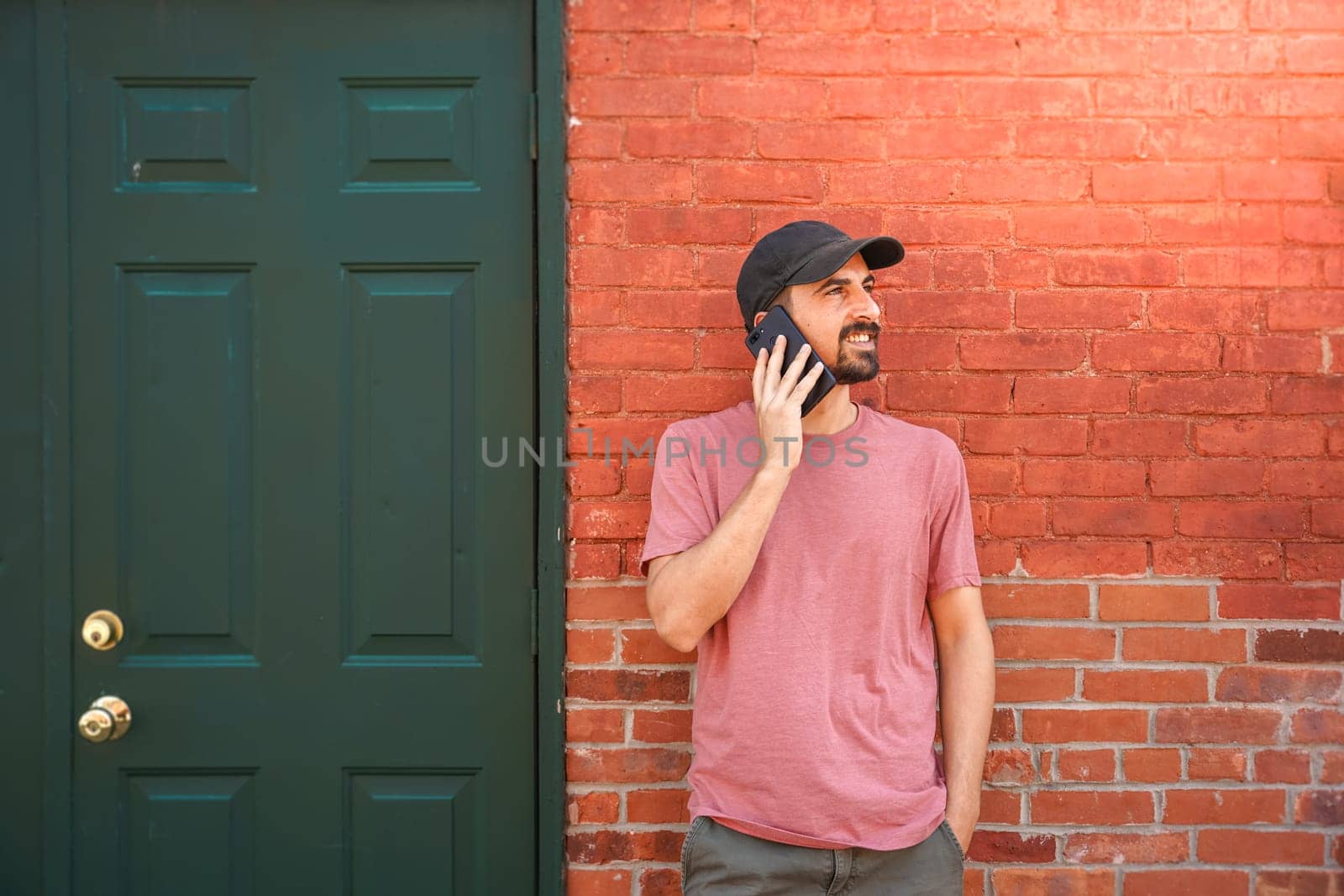 Young man talking with smartphone in front of a brick wall building in the city. . High quality photo