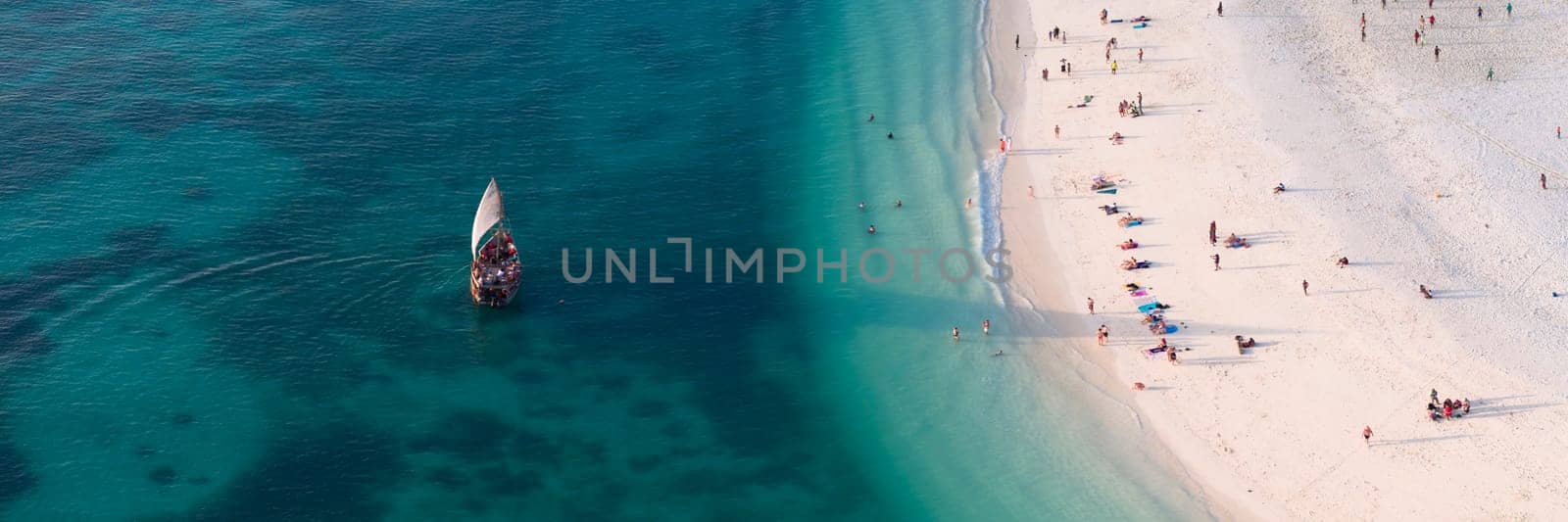 Drone view of dhow boat in the green ocean and wonderful white sandy beach, a beach there are many people, Zanzibar in Tanzania.