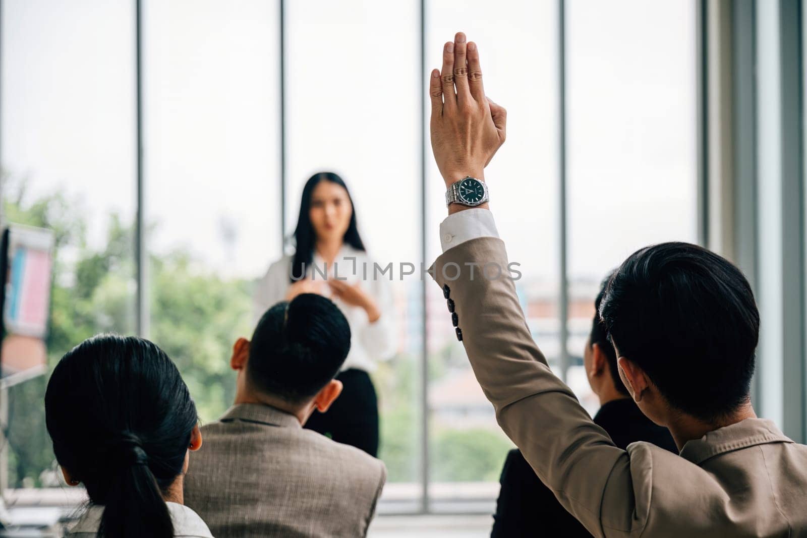 In a seminar classroom at a conference, a large group raises hands in participation. The engaged audience holds the answers, symbolizing collaborative learning. by Sorapop