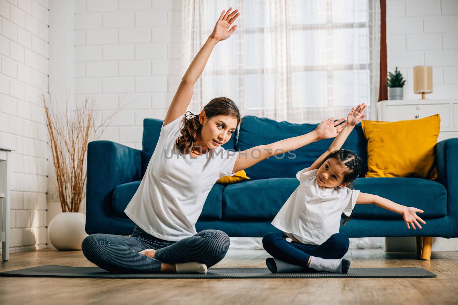 A mother teaches her daughter yoga focusing on stretch and balance in their home. Their smiles reflect the family's togetherness trust and joyful learning.