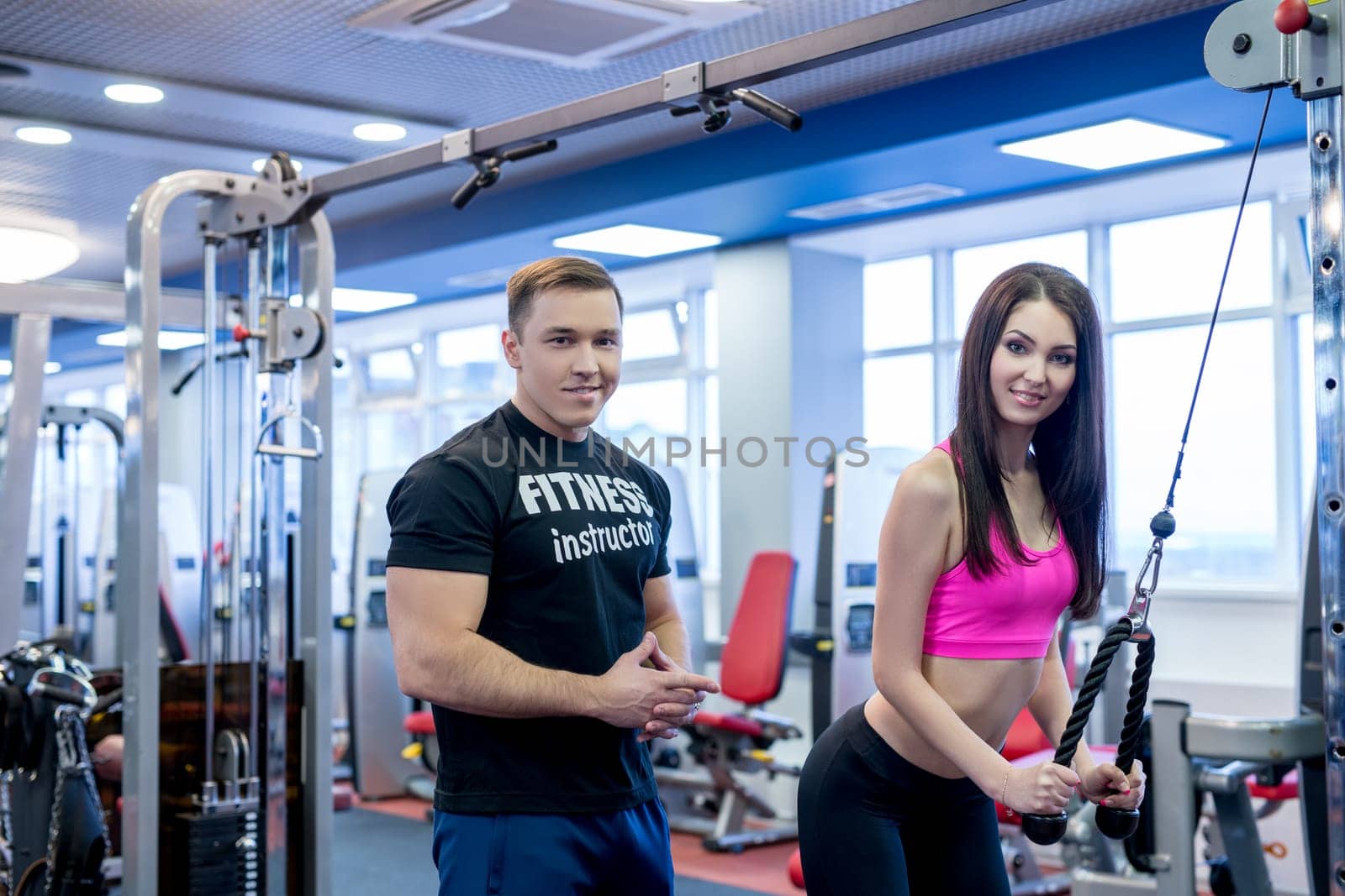 In gym. Image of fitness instructor helping pretty woman