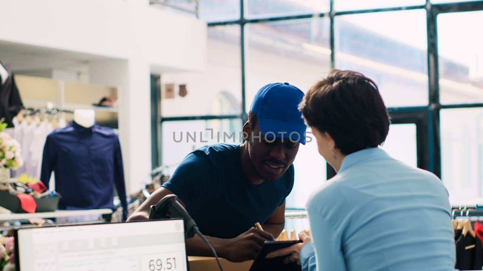 African american deliveryman carrying carton boxes, signing shipping report on tablet computer discussing orders distribution with manager. Store employee working in modern boutique