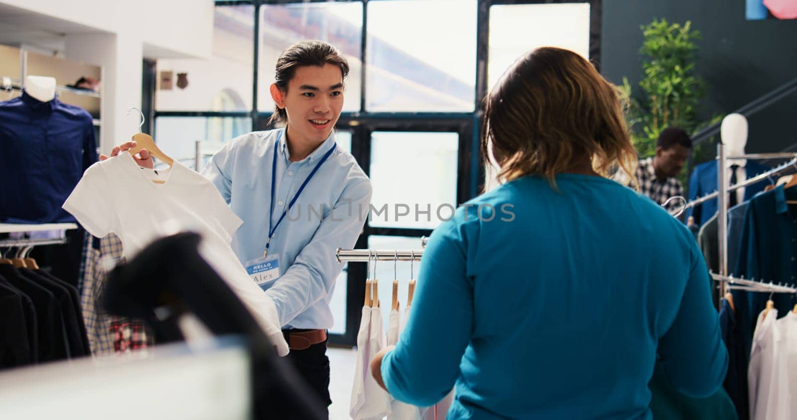 Asian worker helping customer to buy trendy clohtes, discussing shirt fabric in modern boutique. African american woman shopping for fashionable merchandise, looking at new fashion collection