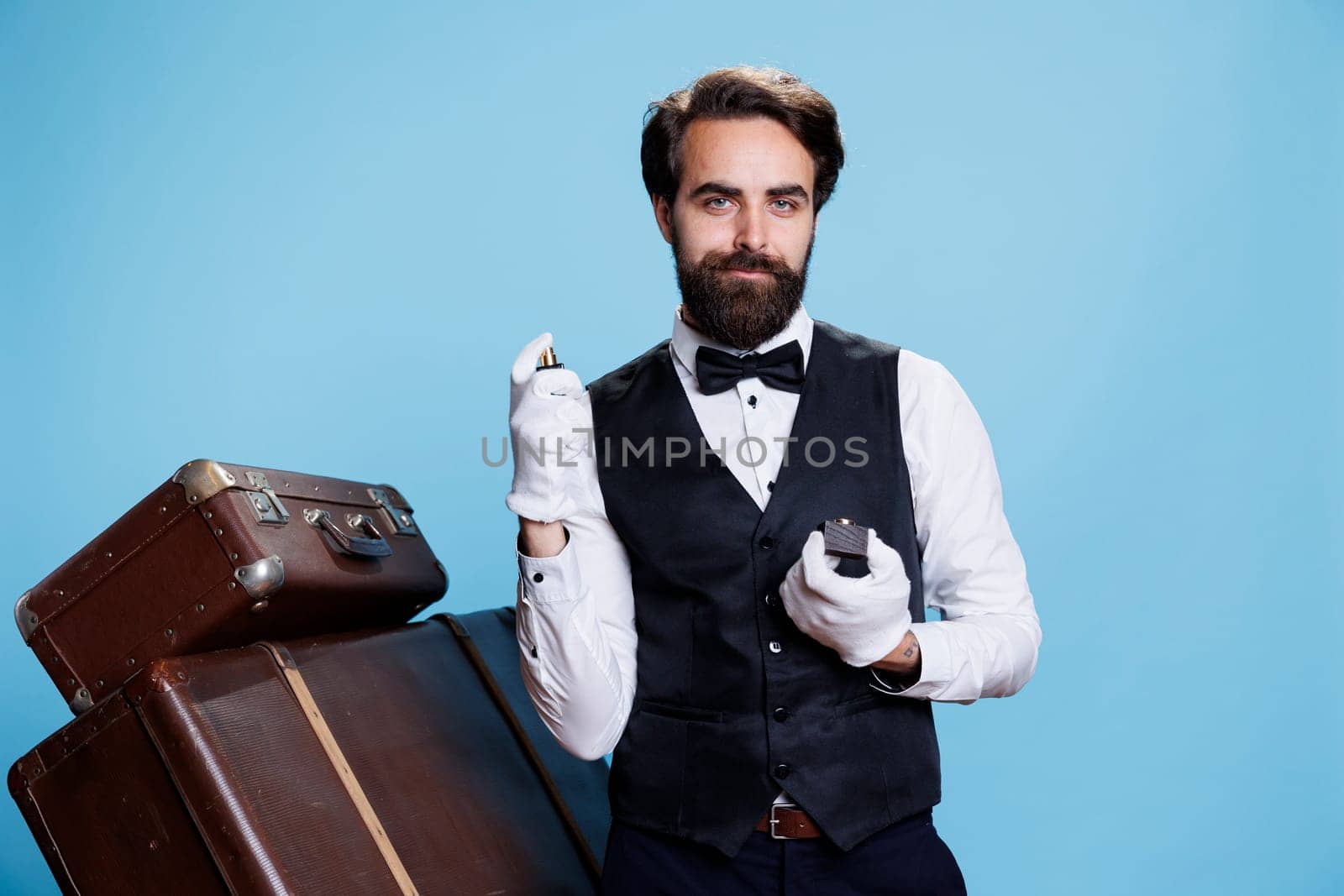 Stylish bellhop applying perfume, using strong bottle of cologne for rich luxurious scent and posing on camera. Professional doorman smelling like aromatic masculine spray, formal clothes.
