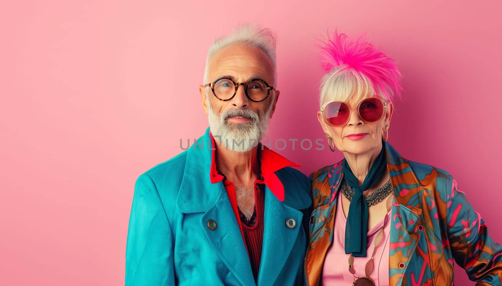 Fashion portrait of stylish modern senior couple together, trendy cool elderly woman and man posing on colorful pink studio background