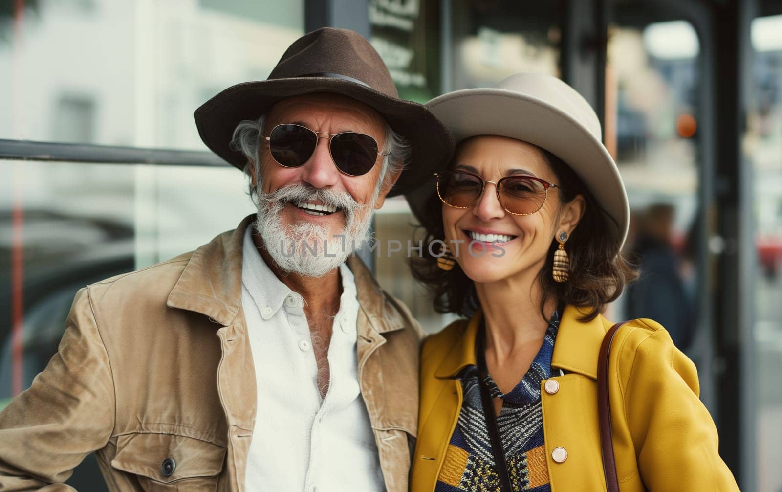 Fashion portrait of stylish happy smiling senior couple together, trendy beautiful elderly woman and man in hats, glasses posing on city street