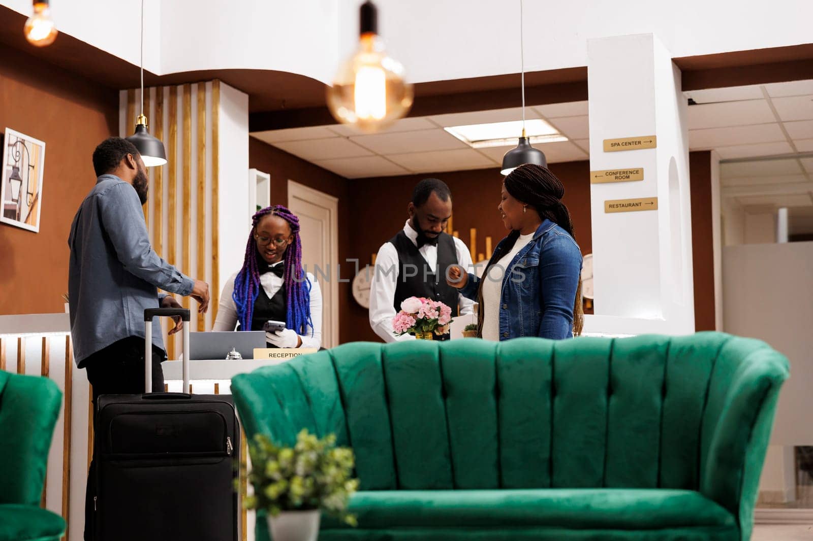 Happy young African American couple checking in at resort, arriving to hotel, traveling together. Friendly front desk staff assisting tourists with check-in process, registering guests