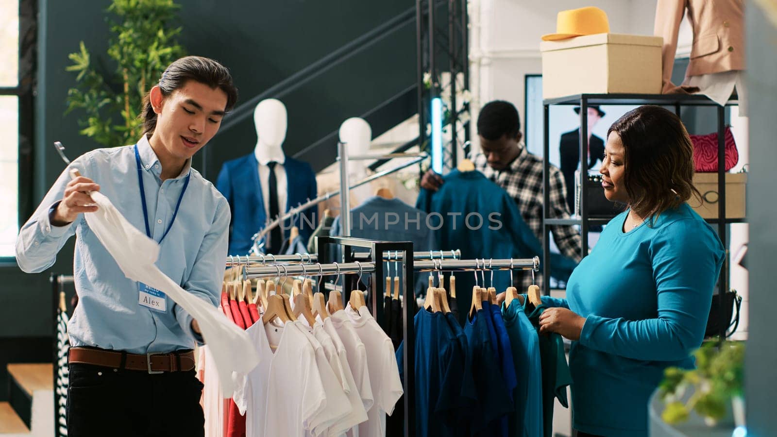 Store manager helping stylish customer with casual wear, african american woman shopping for trendy merchandise. Asian employee arranging fashionable clothes in modern boutique. Fashion concept