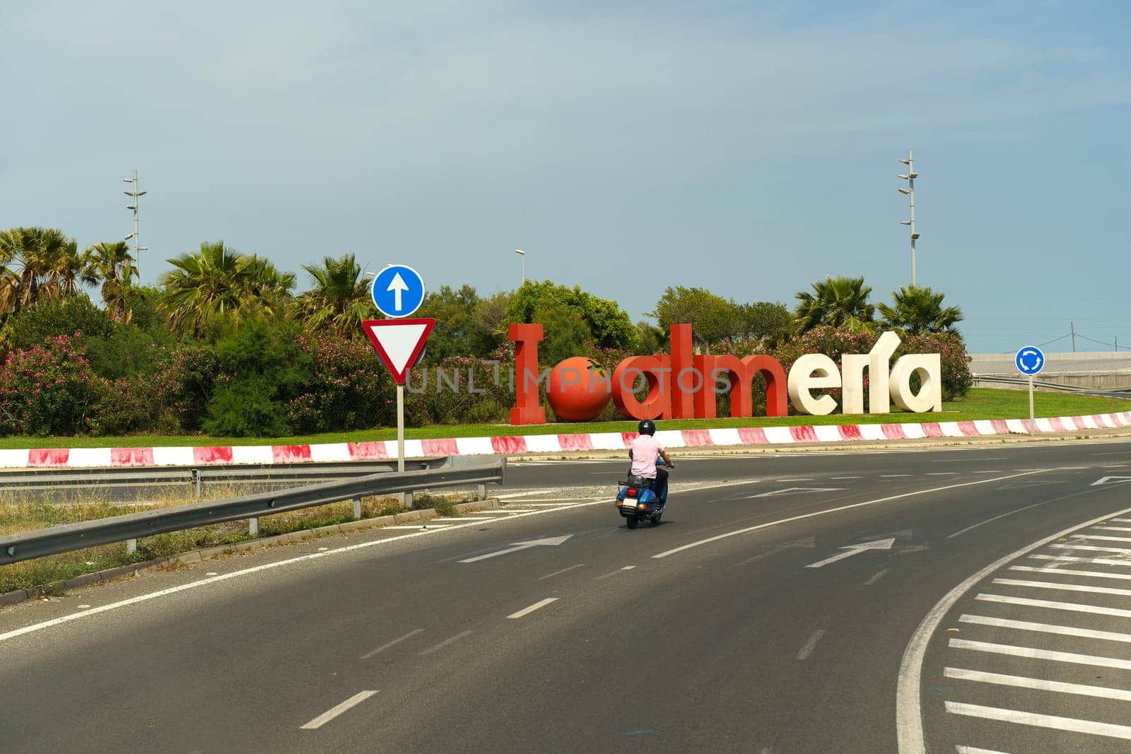 Almeria, Spain - May 25, 2023: A man wearing a helmet is riding a motorcycle down a street lined with buildings, passing by a sign. The scene captures the movement and urban setting.