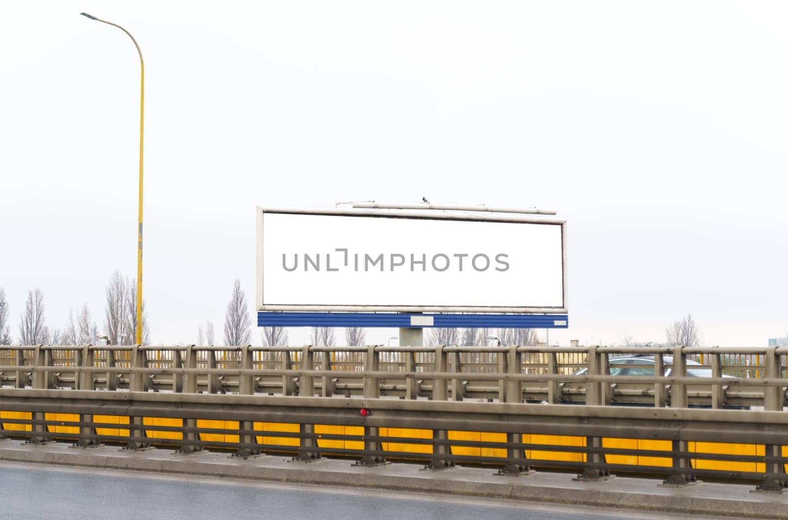 A wide white billboard with a mockup advertisement stands prominently on the side of a busy highway.
