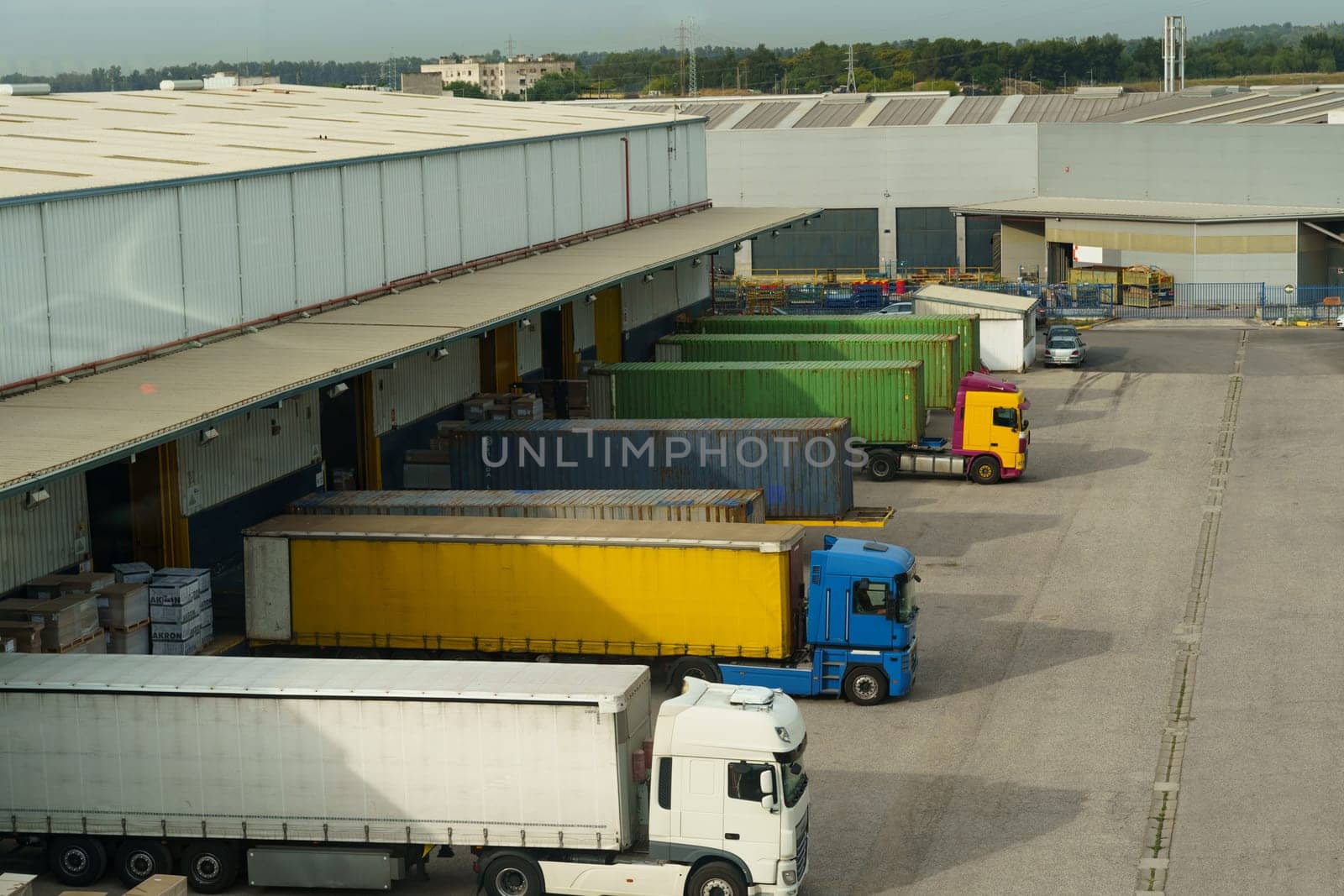 Trucks docked at a cargo bay with colorful freight containers, facilitating logistics and transport at a warehouse facility.