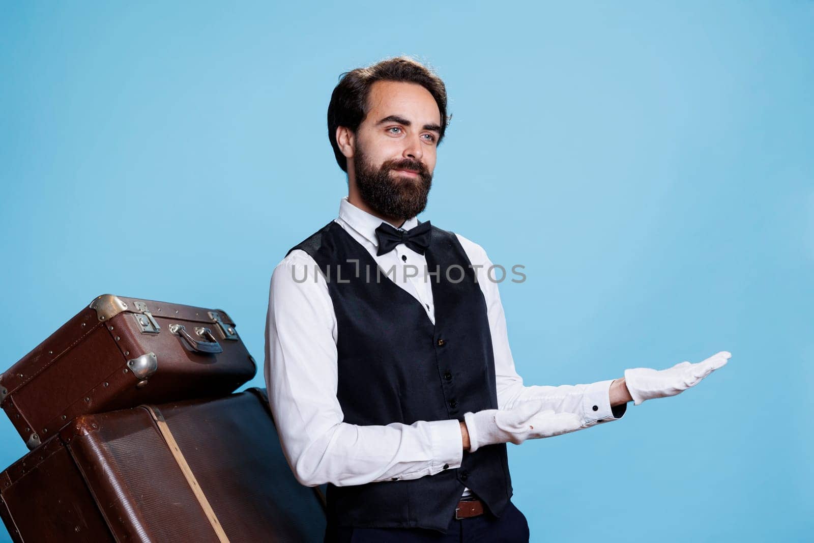 Hotel porter shows left side on camera, wearing professional suit and gloves while he does an advertisement, suggesting direction sideways. Elegant doorkeeper presents ad in studio.