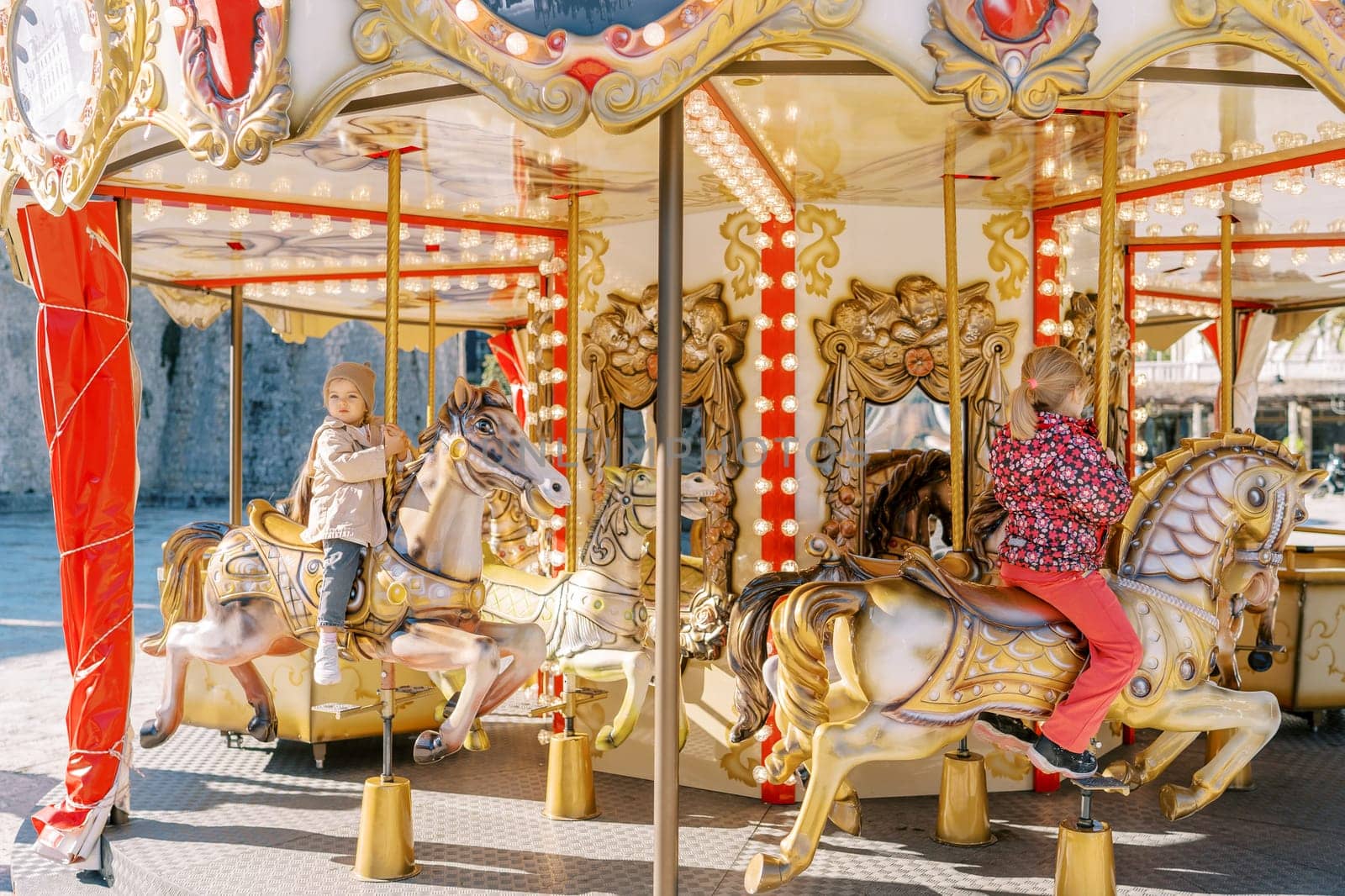 Little children ride colorful toy horses on a carousel while holding onto a pole by Nadtochiy