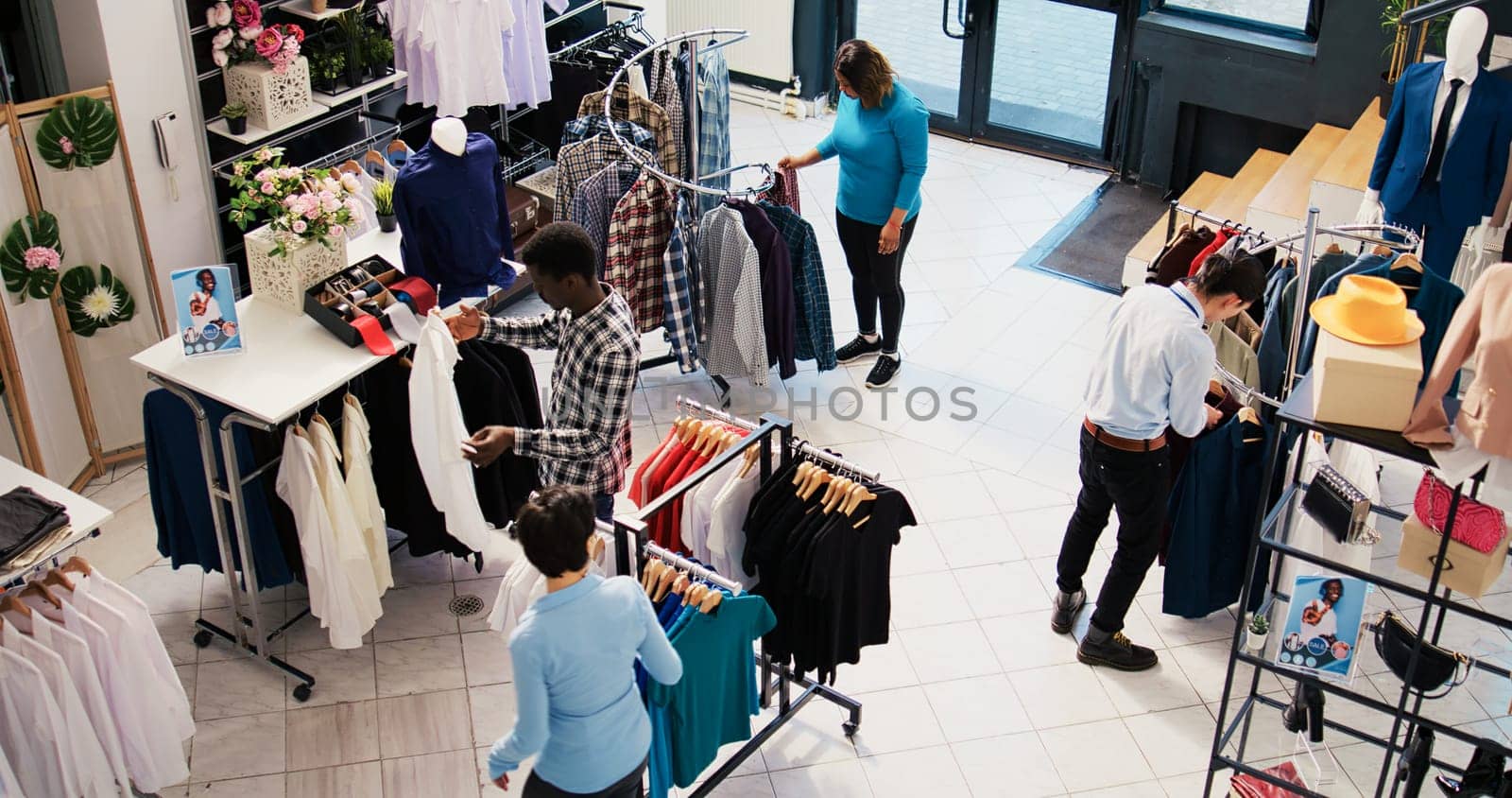 Top view of diverse customers checking stylish clothes, shopping for fashionable merchandise and accessories in modern boutique. Clients analyzing hangers with new fashion collection
