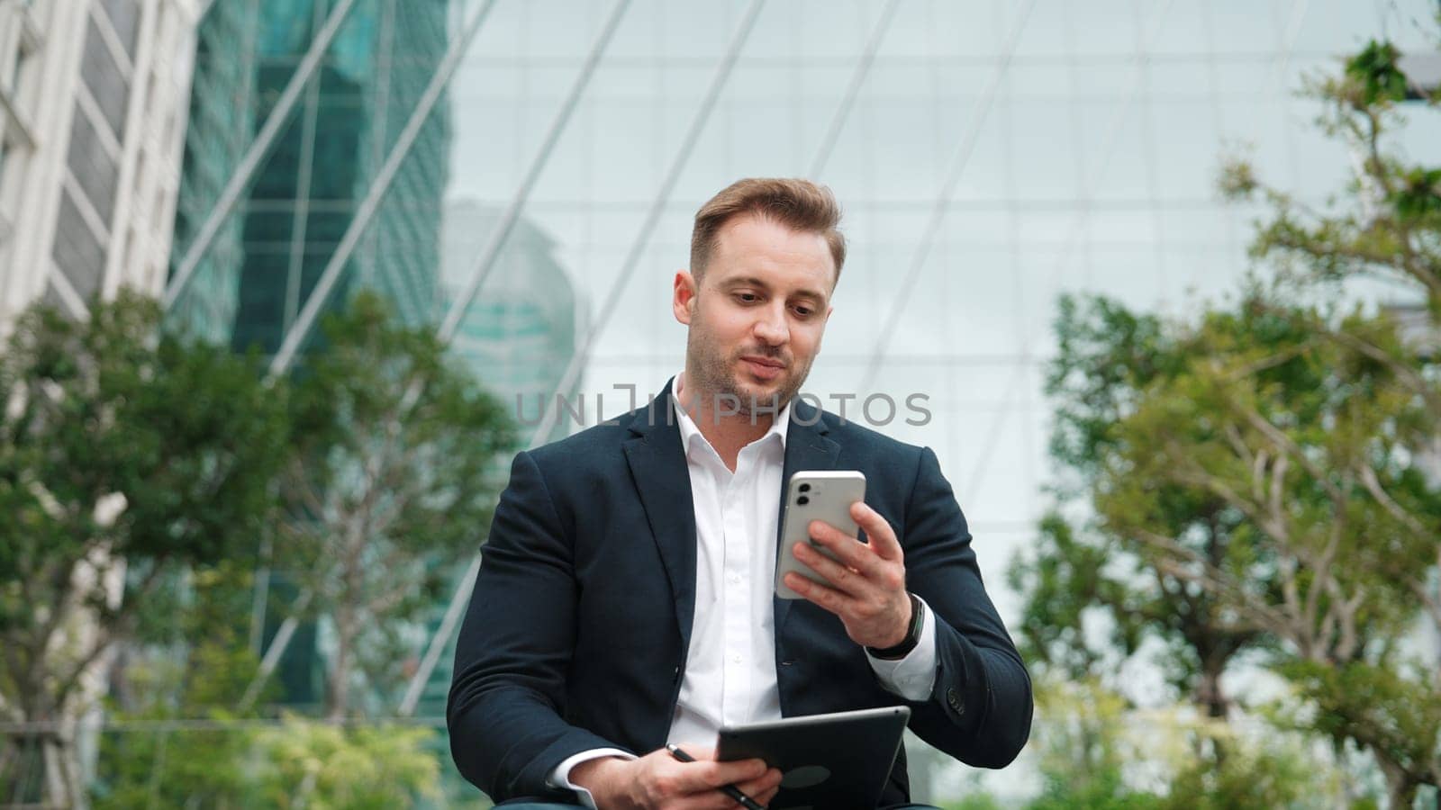 Front view of businessman sitting at park while talking to investors about marketing strategy. Caucasian executive manager looking increasing sales or successful project at eco city. Lifestyle. Urbane