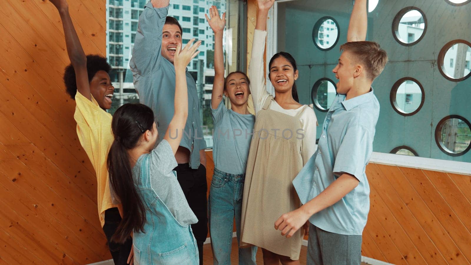 Smart teacher and diverse student standing while putting hand in the air to celebrate successful project.. Skilled instructor with highschool children with mixed races in casual outfit . Edification.