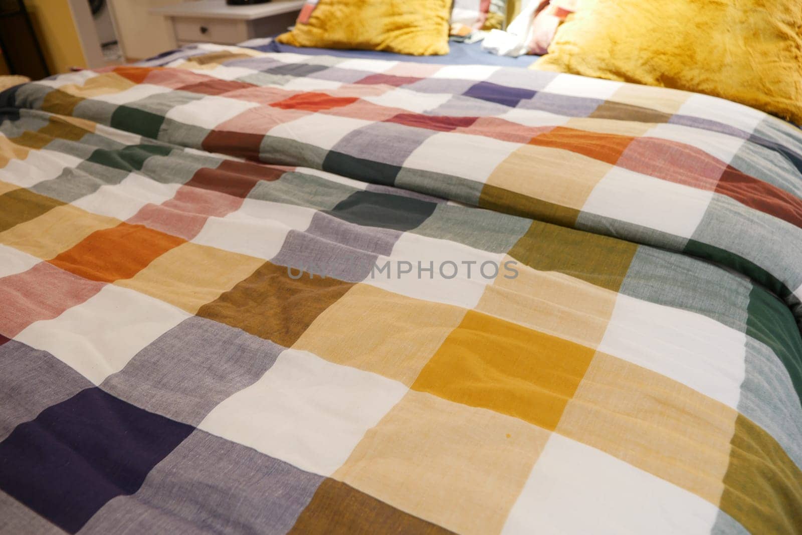 a bed with a colorful plaid comforter and pillows in shades of Purple, Orange, and Yellow