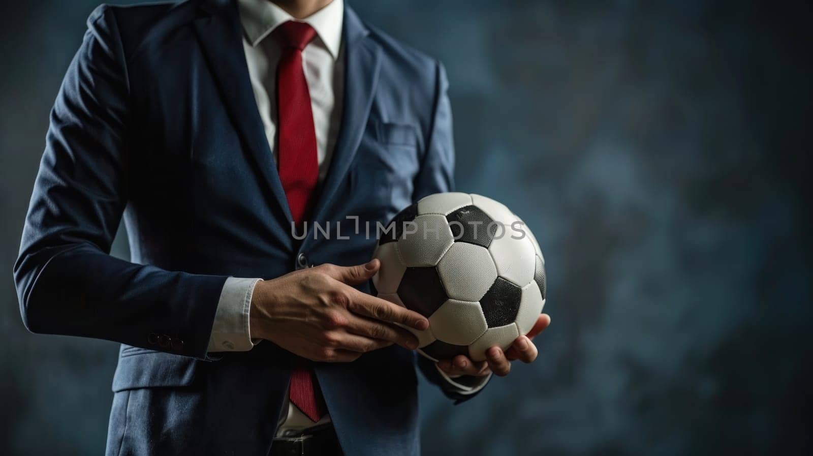 A football manager wear suit and red tie hand holding football.