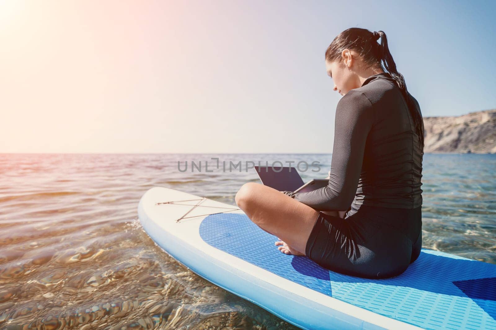 Woman sea laptop. Digital nomad, freelancer with laptop working on sup board at calm sea beach. Happy smiling girl relieves stress from work. Freelance, digital nomad, travel and holidays concept by panophotograph