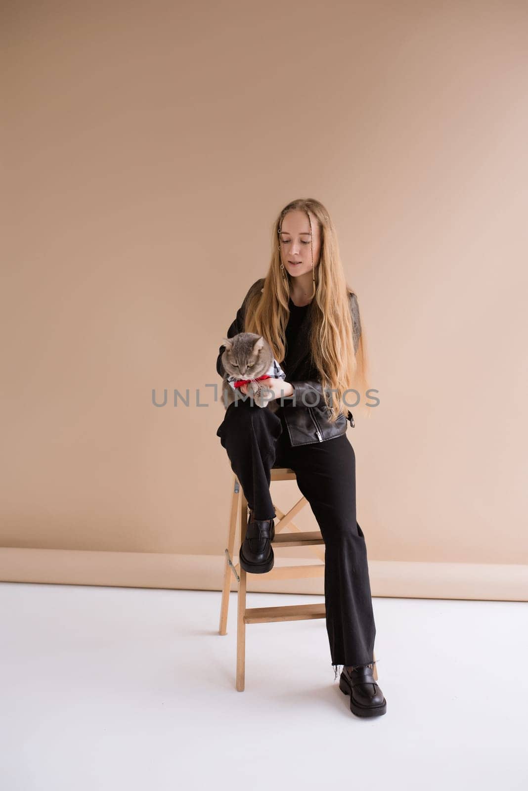 A woman natural blonde long hair smiling in a black clothes, sitting on photo studio. girl with pet scottish straight cat. portrait , vertical,