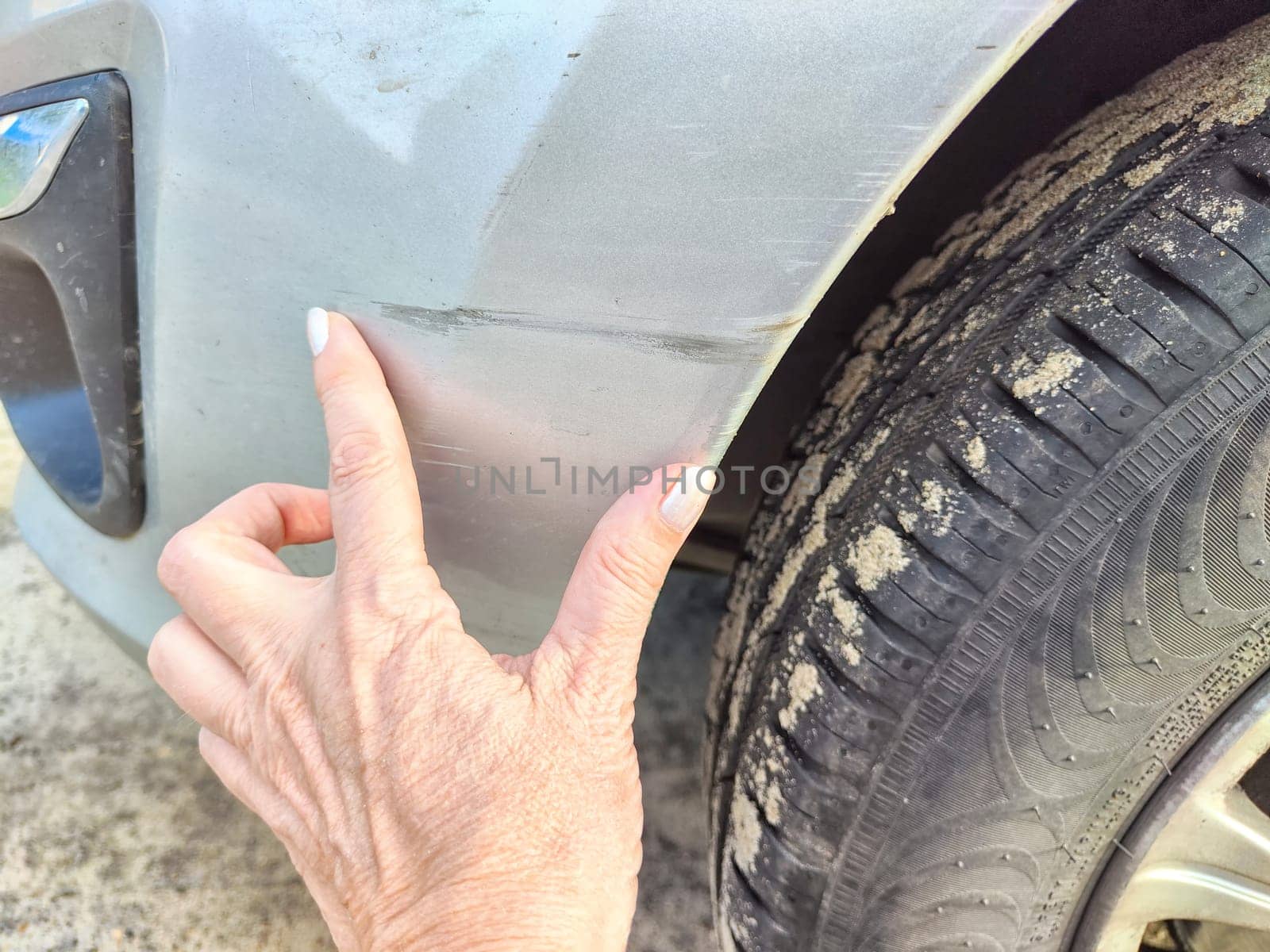 Finger indicating a scratch on a vehicles fender. Close-Up of a Scratched Car Fender With Finger Pointing by keleny