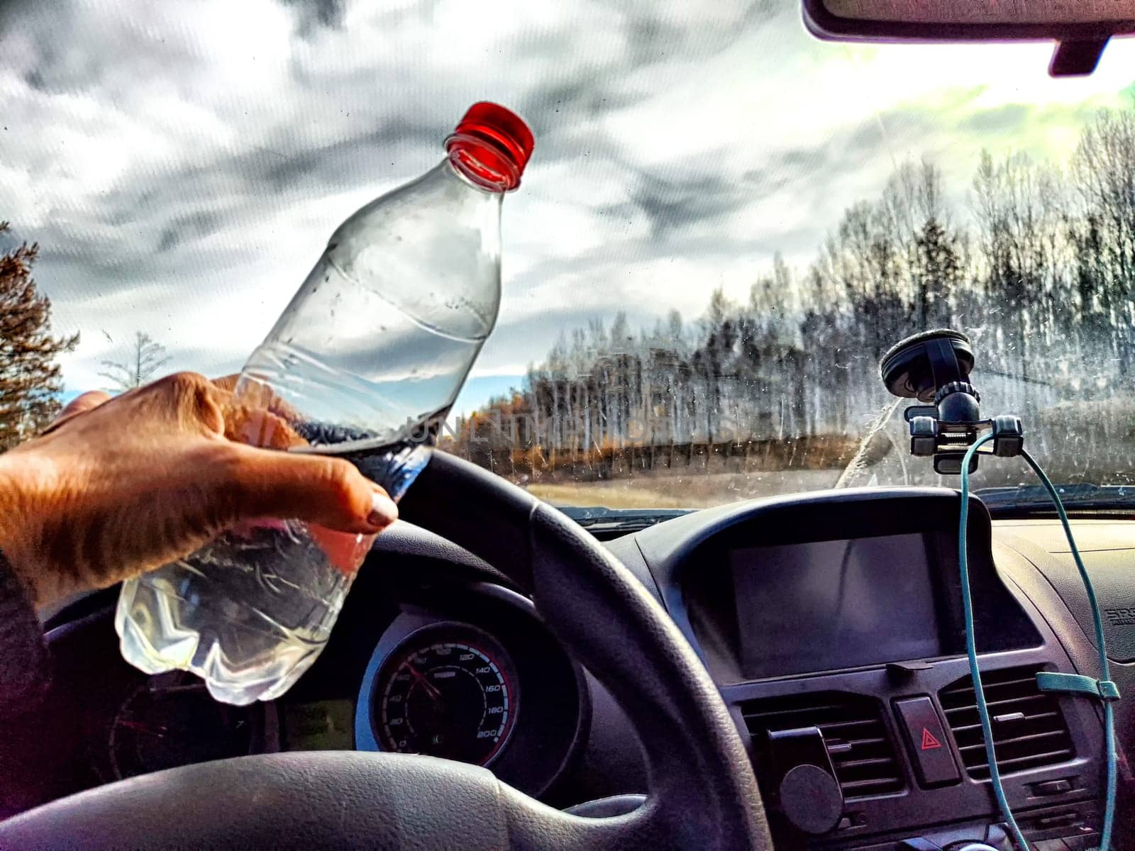 Driver Holding Water Bottle During Road Trip. Hand holding a water bottle in car with view of road. Ability to stay awake while driving for long time by keleny