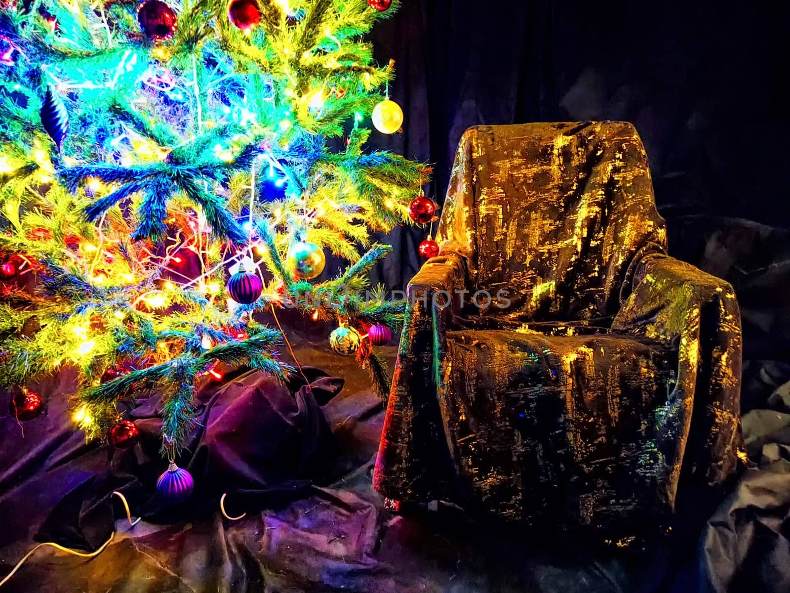 A beautifully decorated Christmas tree next to a luxurious chair. Festive Christmas Tree With Illuminated Lights Beside an Ornate Chair by keleny